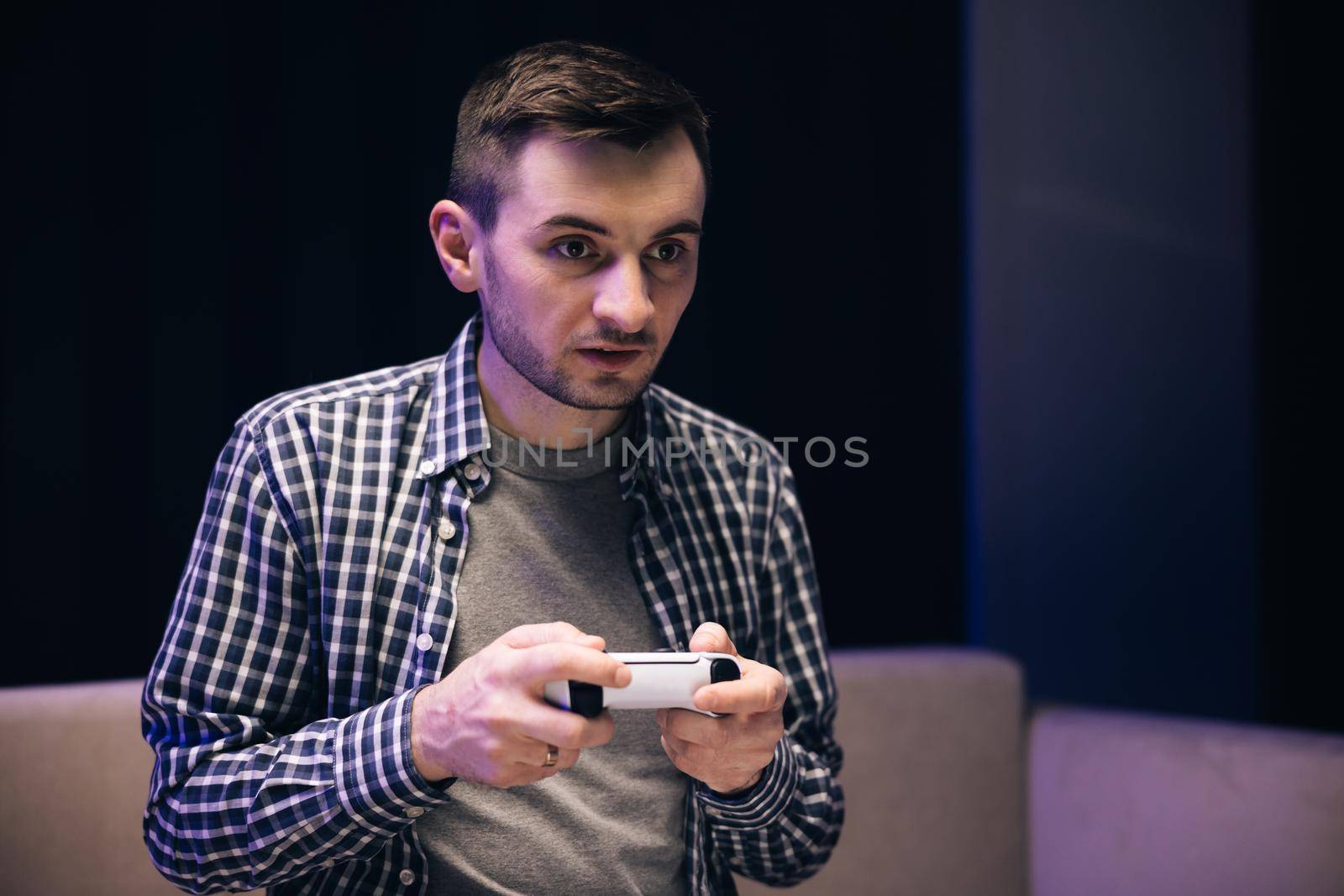 Caucasian guy playing video game and using joystick . Handsome young man enjoying free time alone while sitting on couch in living room by uflypro