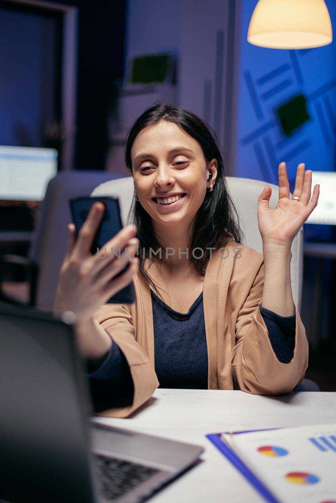 Saying hello in the course of teleconference with entrepreneurs doing overtime. Woman working on finance during a video conference with coworkers at night hours in the office.