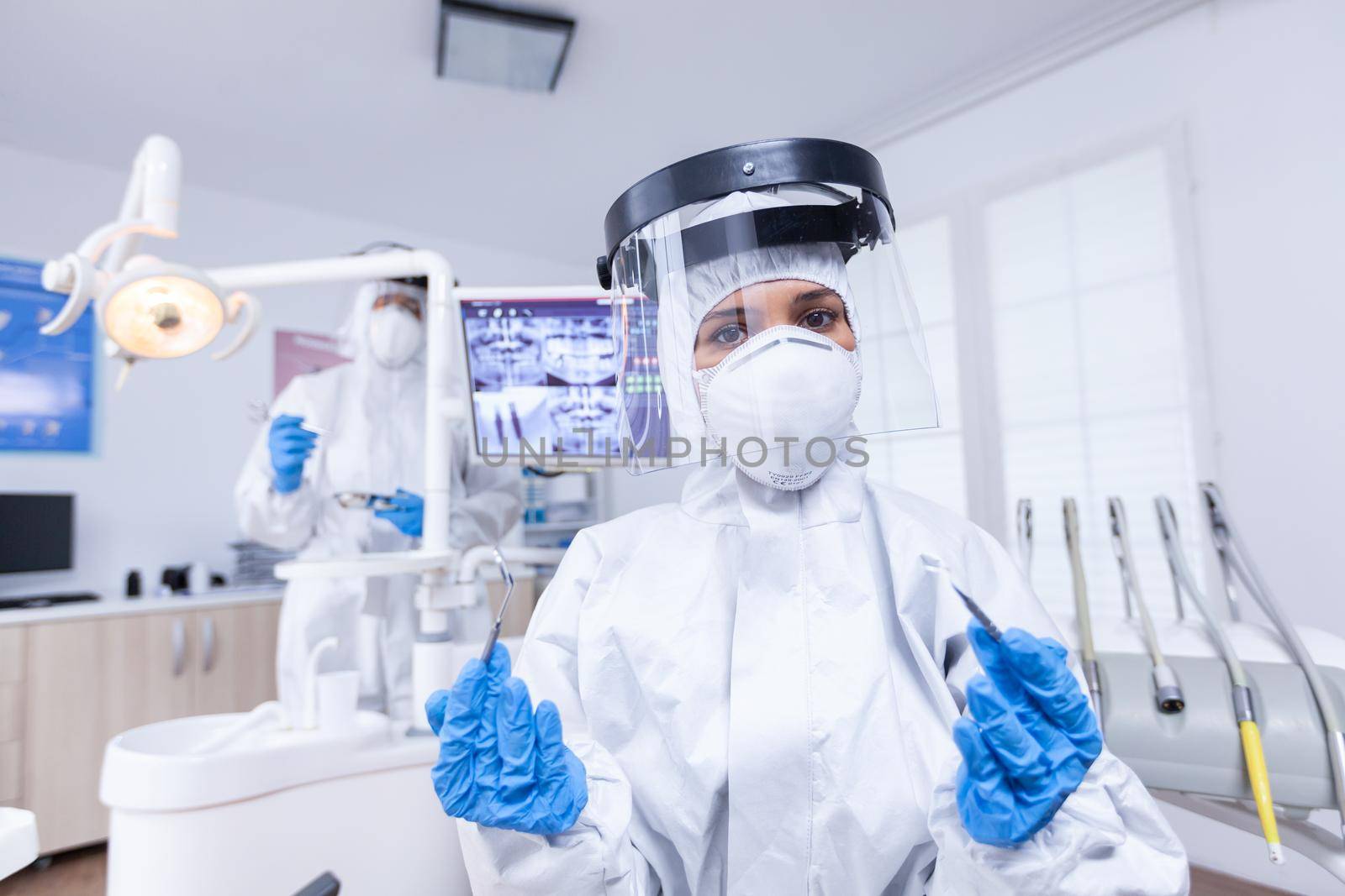 Patient pov of dentist in covid protectiv suit with her tools in dental office. Stomatolog wearing safety gear against coronavirus during heatlhcare check of patient.