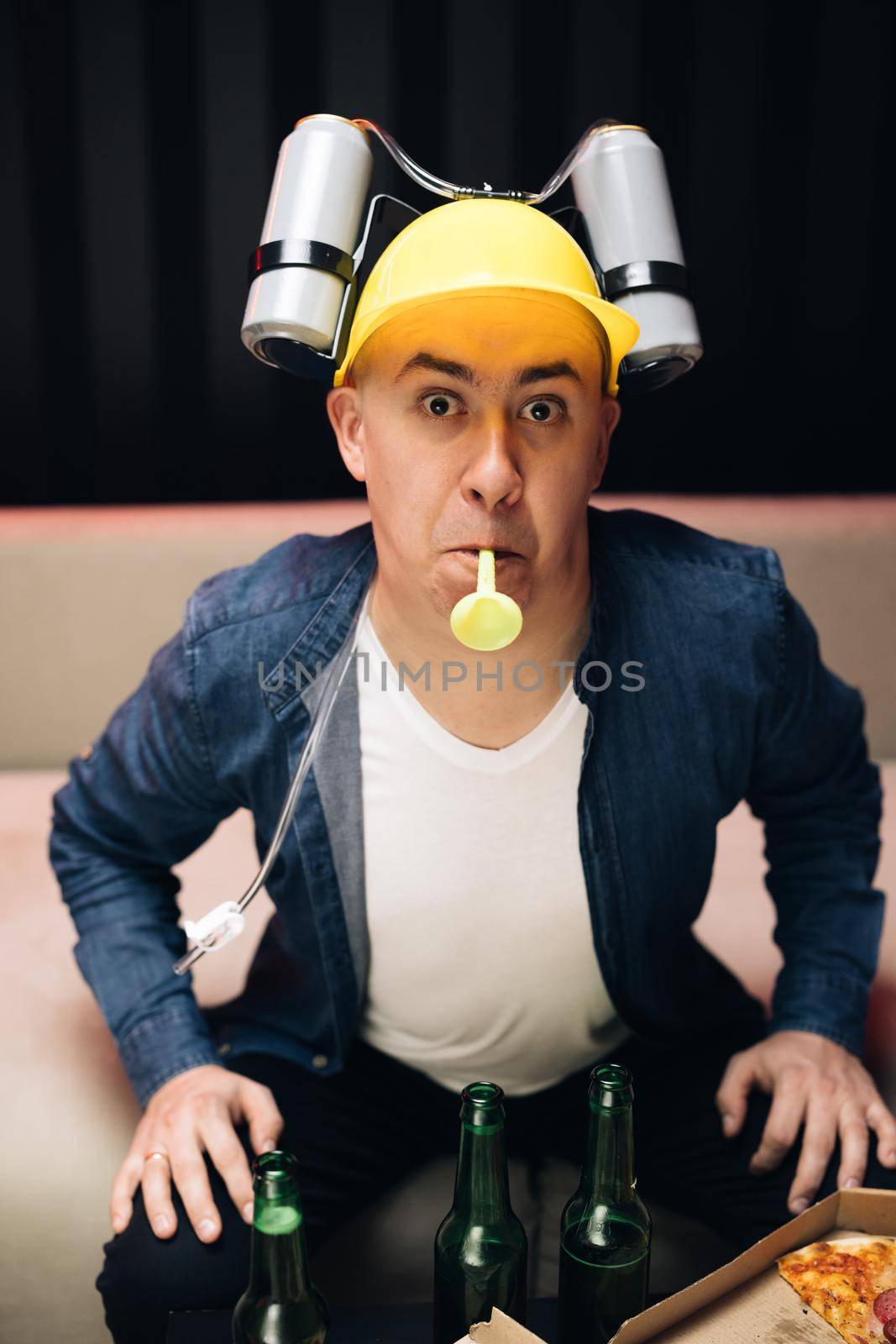 Man sitting on the couch at night in beer helmet and watching TV. Screaming and rejoicing. Football fan screaming and watching match at home by uflypro