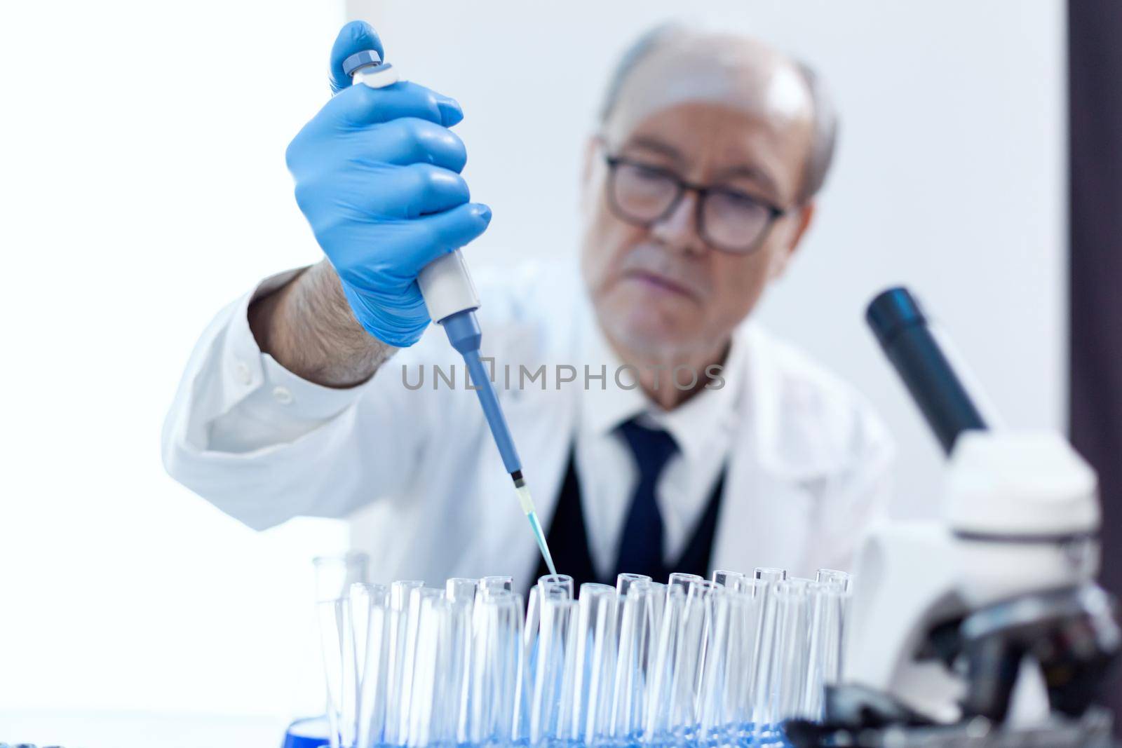 Chemist scientist working with dropper pipette and blue substance in modern laboratory. Senior professional chemist using pippete with blue solution for microbiology tests.
