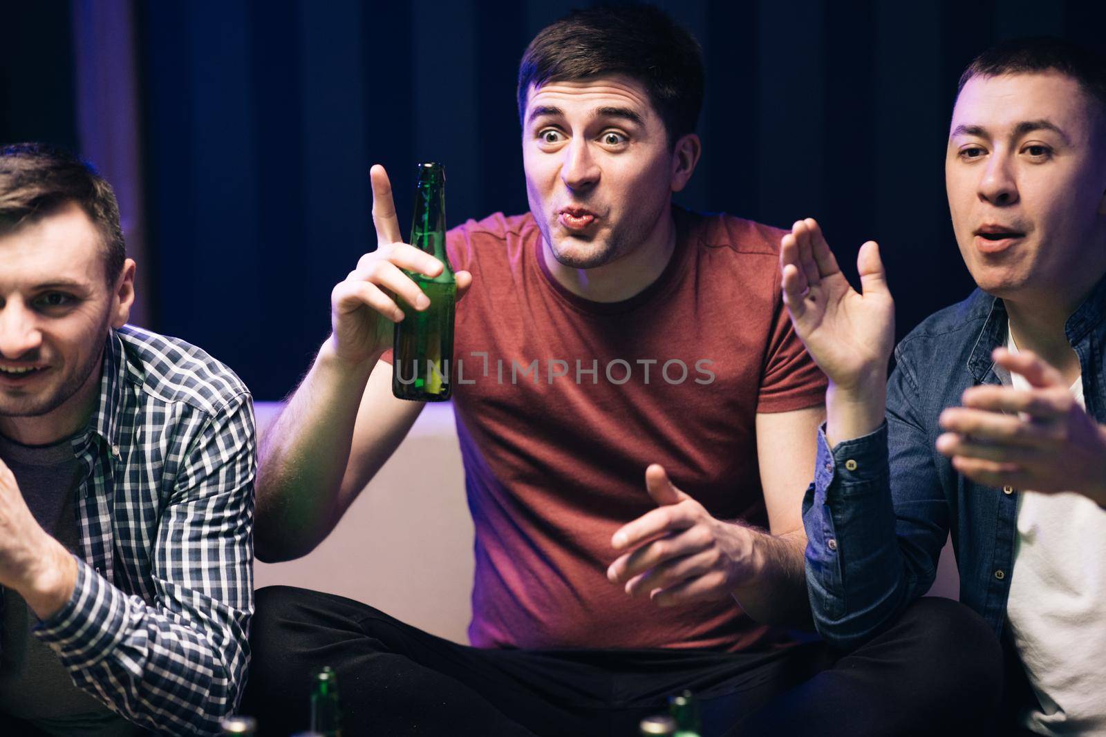 Men watching TV with sport channel late at night and drinking beer. Cheerful happy Caucasian guys cheering for favorite team. Loyal football fans supporting their team by uflypro