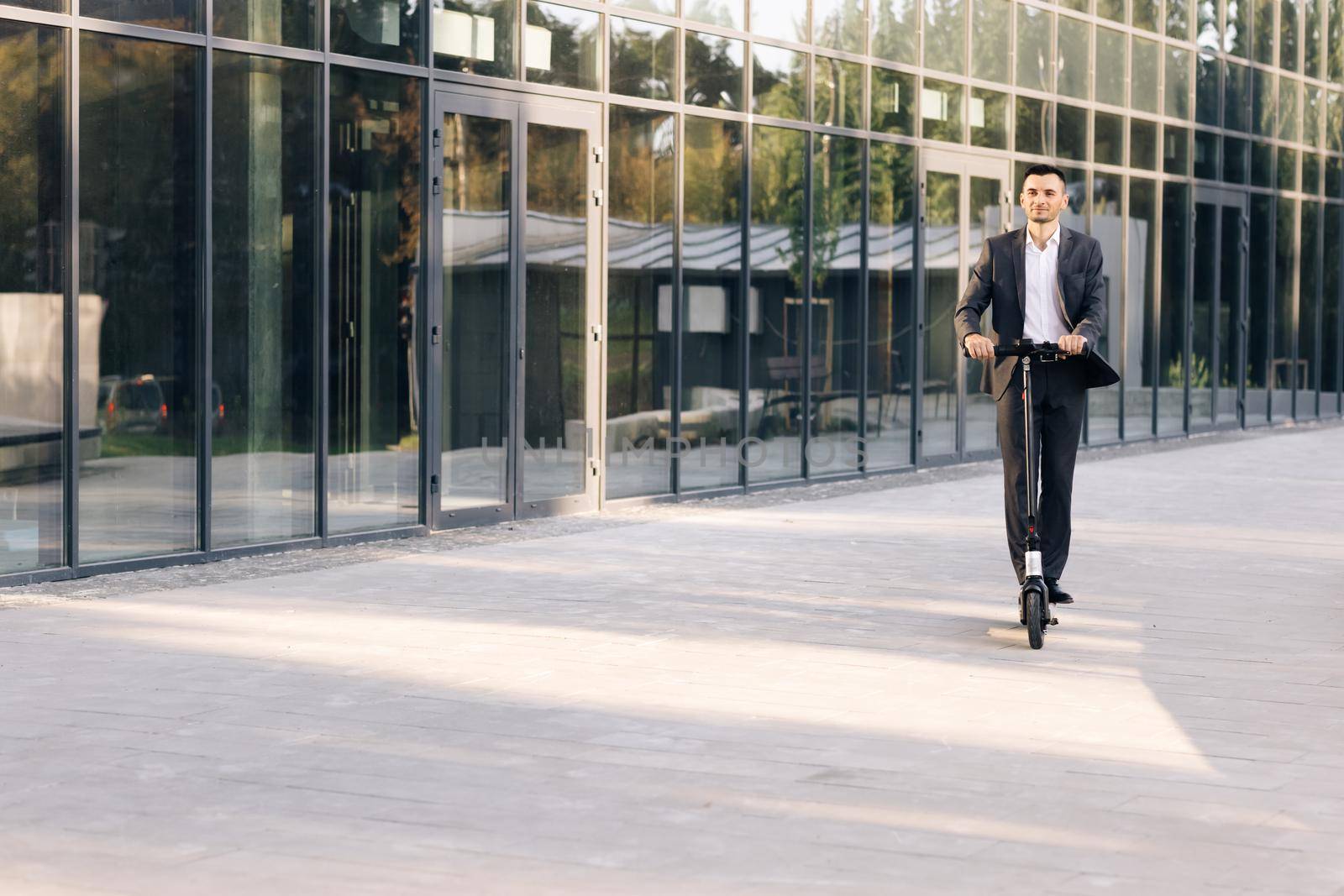 Man rides an electric scooter on the road. Modern way of getting around. Handsome man in a suit riding electric scooter in a city. Adult businessman riding with electric scooter to work by uflypro
