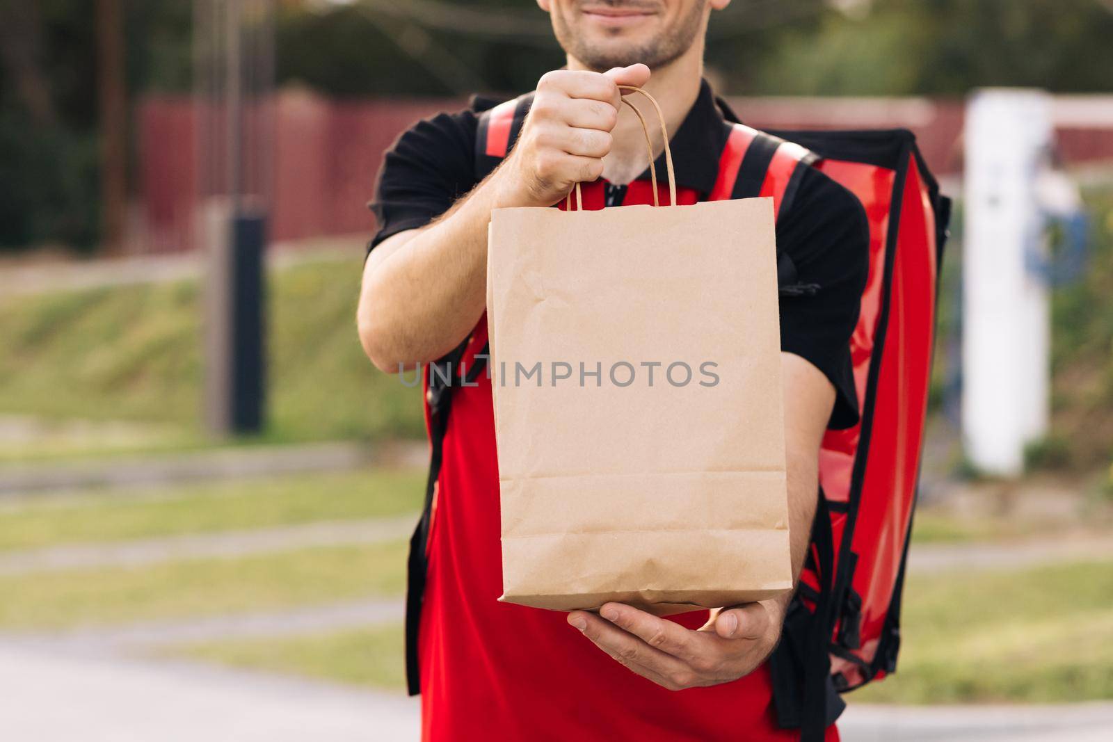 Food delivery man order from a restaurant. Handsome young man in a T-shirt and a cap. Happy delivery worker holding packet with food smiling. Delivery service door to door.