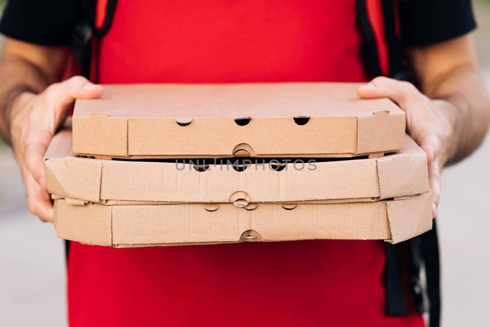 Close-up of the couriers hands and pizza. Portrait of delivery man holding cardboard pizza box against city, courier food delivery. Delivery man holding boxes with hot pizza, food order online.