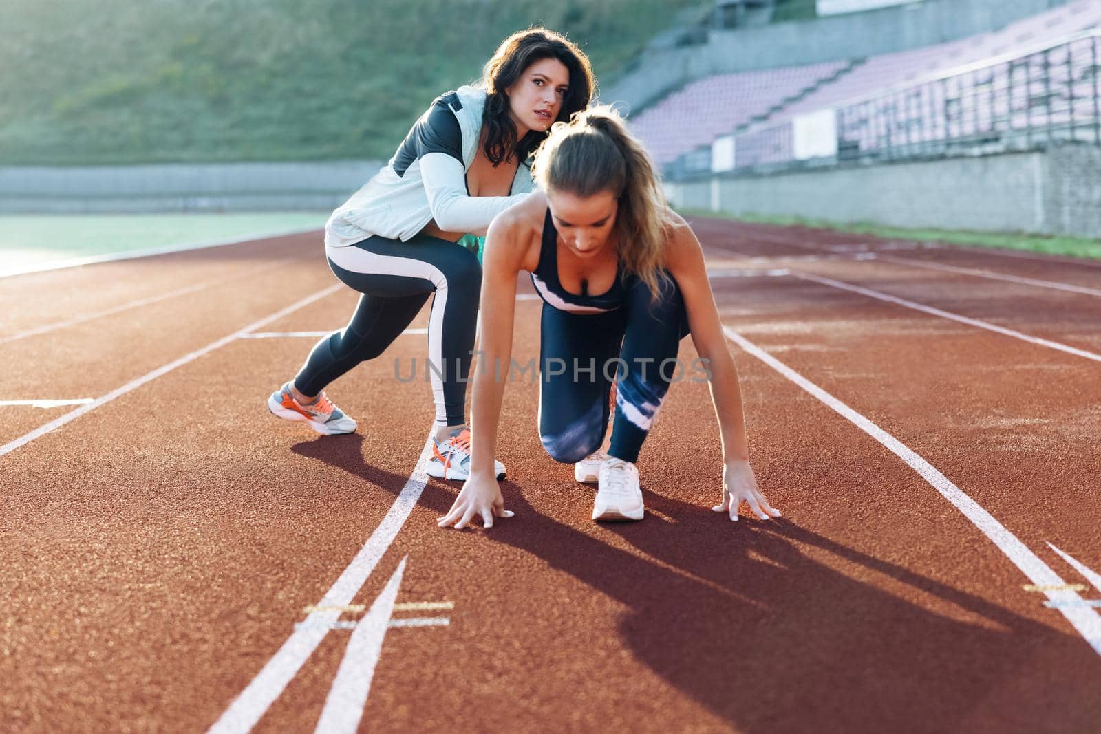 Young athlete exercises with personal trainer standing on start on stadium, then rushing forward, getting ready for competition. Female athlete on track. Exercising strength, cardio and power