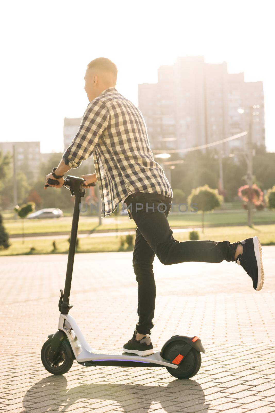 Hipster man commuting to work through city on electric scooter. Eco-friendly transportation. Fast speed driving electric transport. Man riding an escooter. Ecology and urban lifestyle by uflypro