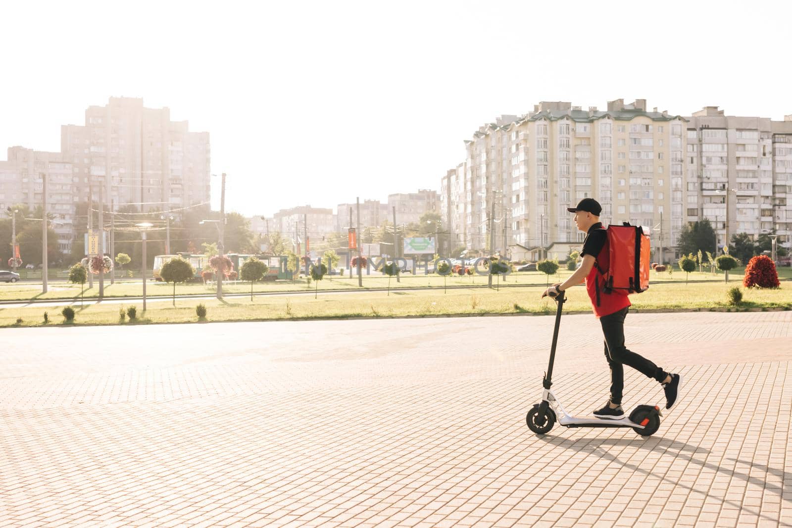 Asian man courier food delivery with red thermal backpack rides the street on an electric scooter deliver online order client customer. Deliveryman worker employee in red uniform. Excellent delivery by uflypro