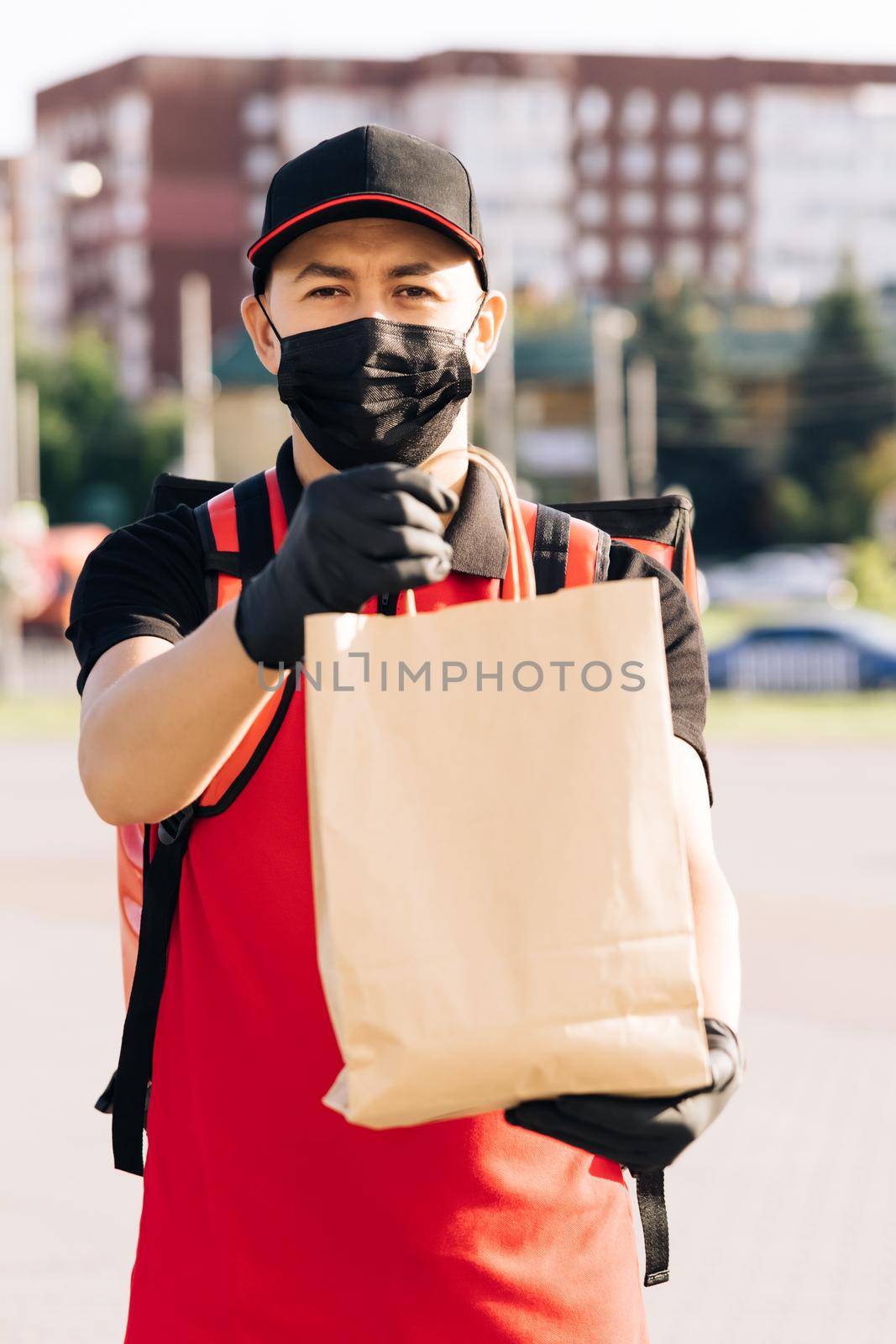 Food delivery man holding paper bag with food at street outdoors home, deliveryman in protective medical face mask gloves, coronavirus COVID-19 epidemic quarantine outbreak. Delivery services.