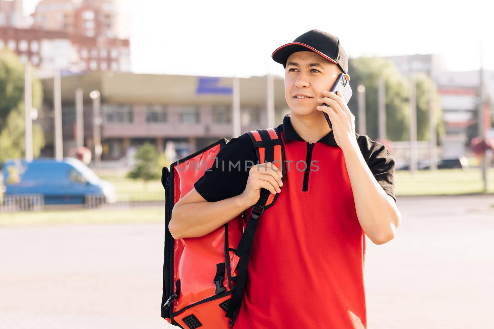 Food delivery guy with red backpack deliver orders. Male courier with isothermal food case box arrives to the entrance to the house and calls for client.