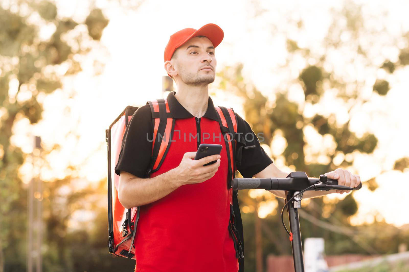 Courier checking customer address on his phone, food delivery outbreak. Food delivery guy with red backpack navigates in phone in city, searching for fast food delivery addresses. Fast delivery.