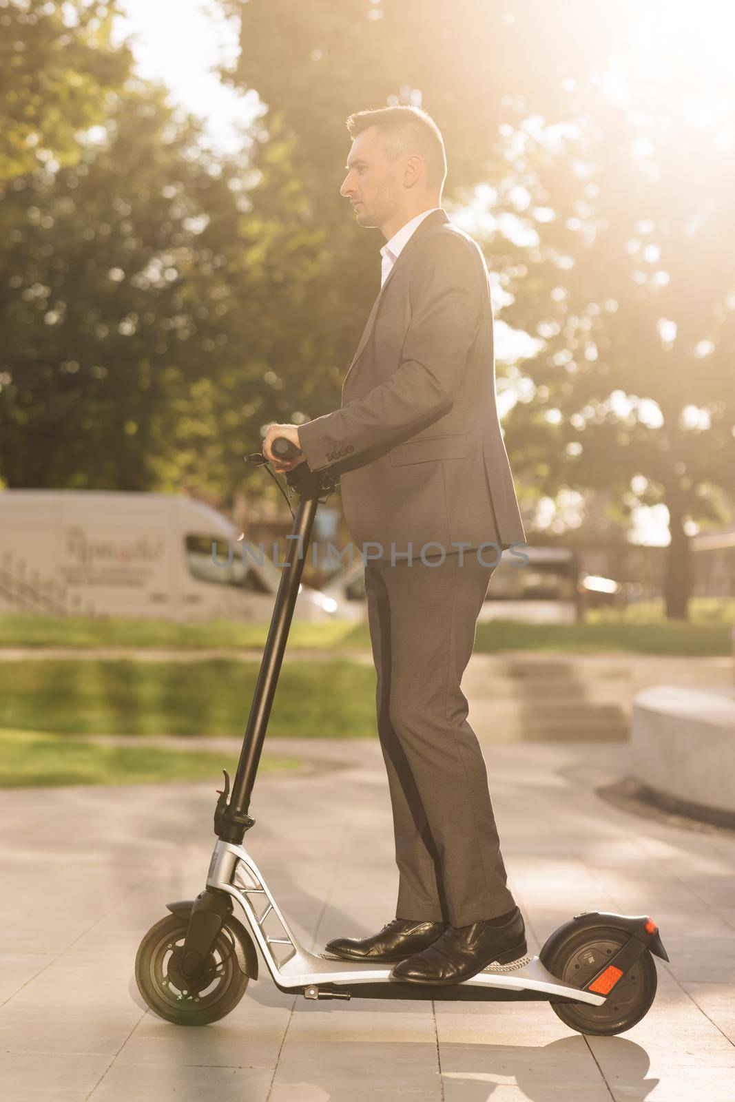 Adult businessman riding with electric scooter to work. Man rides an electric scooter on the road. Modern way of getting around. Handsome man in a suit riding electric scooter in a city. by uflypro