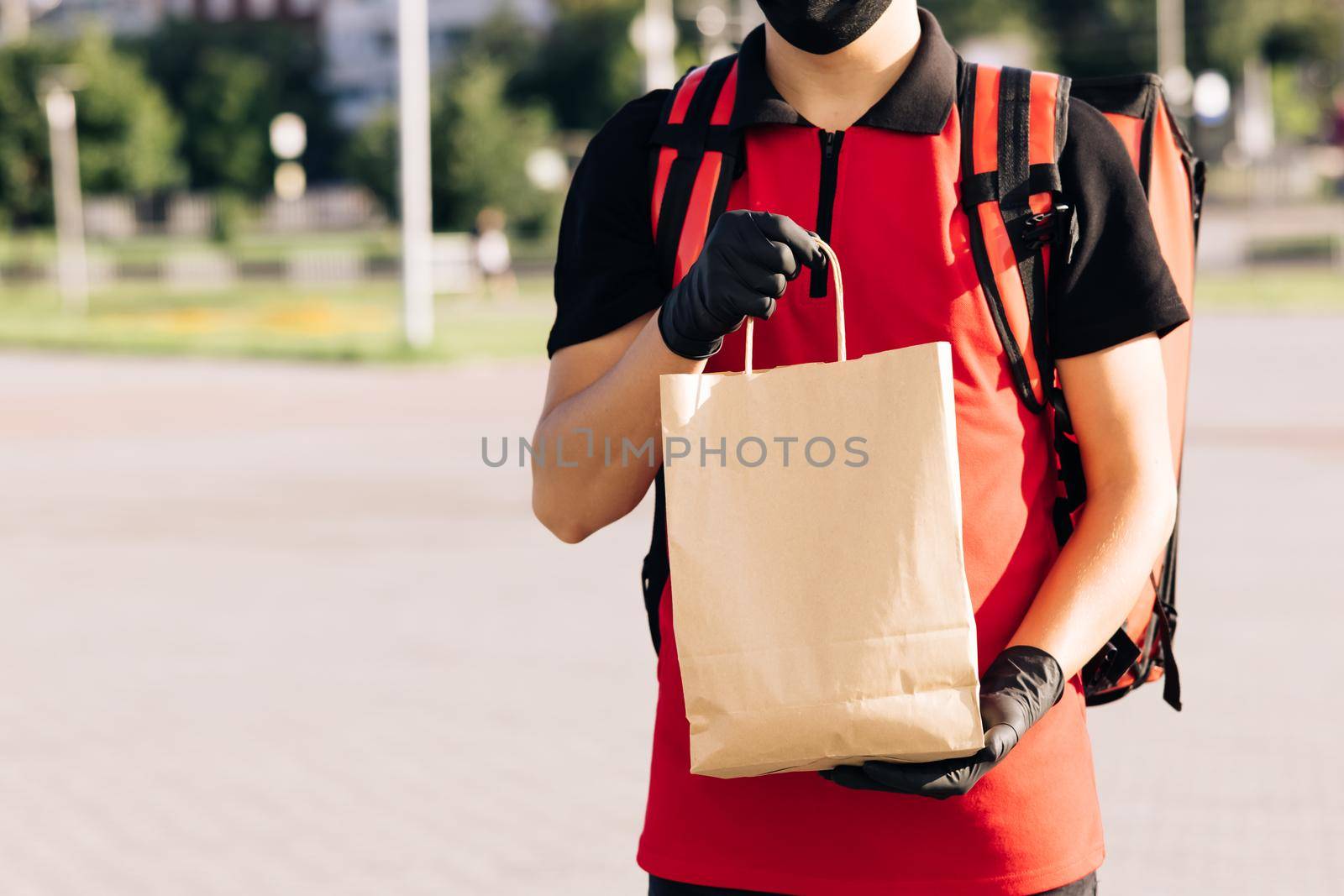 Food delivery man holding paper bag with food at street outdoors home, deliveryman in protective medical face mask gloves, coronavirus COVID-19 epidemic quarantine outbreak. Delivery services by uflypro