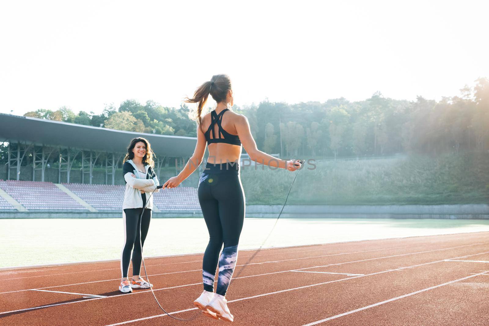 Caucasian woman with personal trainer jumping rope as part of her fitness workout. Sporty female with a good figure jumps rope on sports track of stadium. Exercising strength cardio and power.