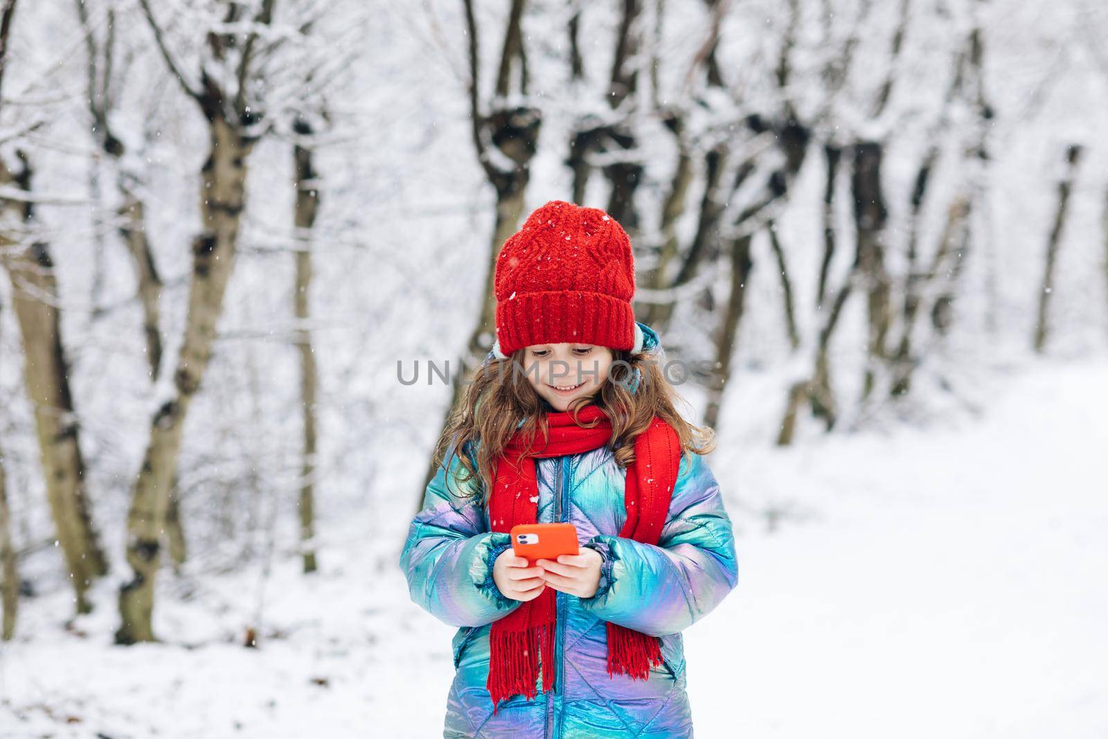 Happy cute little kid use smart phone funny face mask app look at cell screen smiles at something funny. Holidays and celebrations concept. Outside. The dead of winter, cold weather, frost, snow. by uflypro
