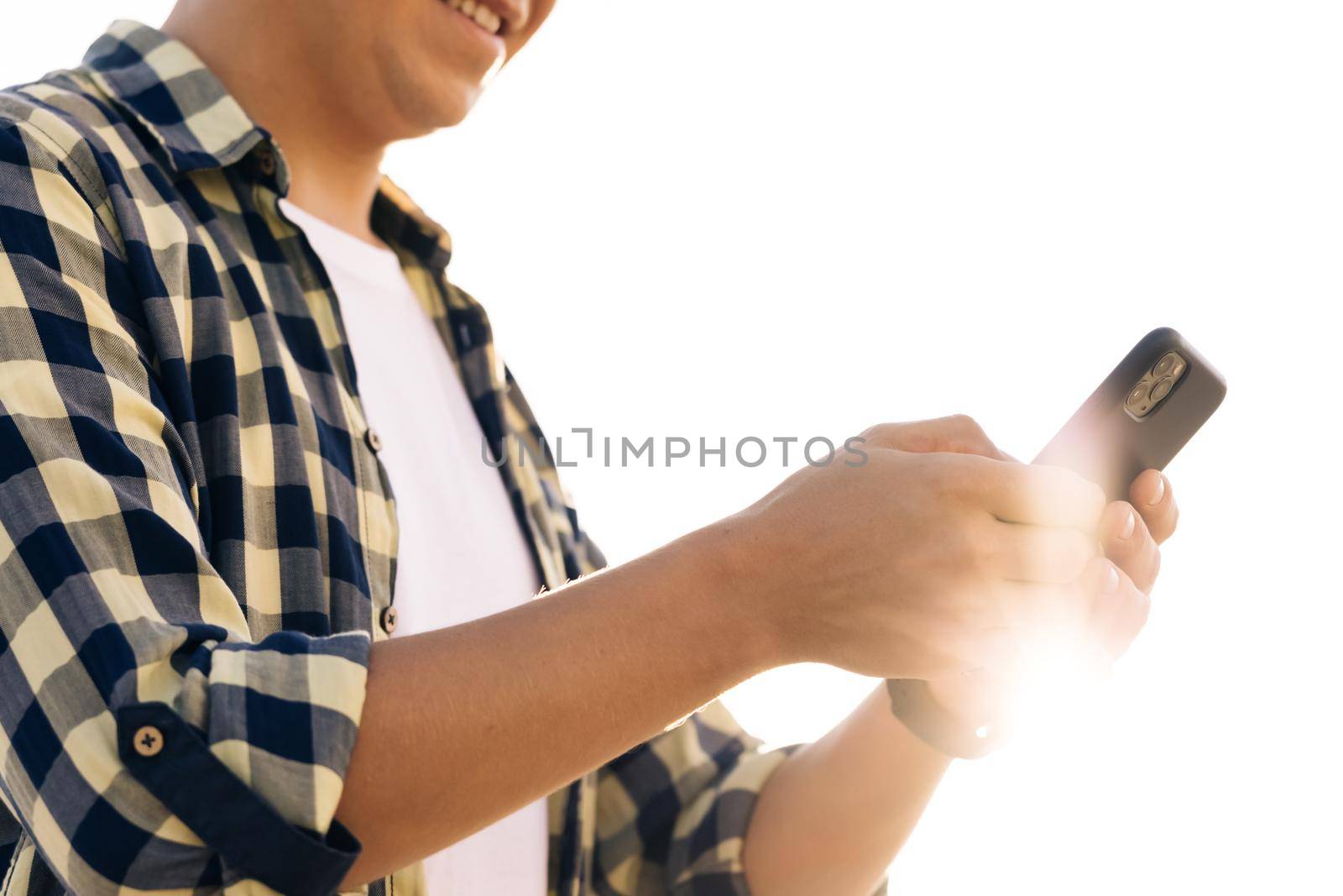 Hipster man in shirt is using a smartphone on a street in downtown. He smiles and looks successful. He's browsing the web on his device.