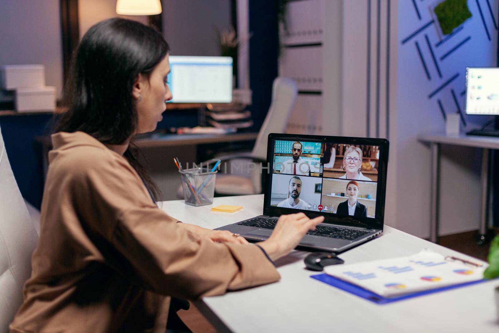 Businesswoman leading a video conference call late night discussing about project deadline. Freelancer working on finance during a video conference with coworkers at night hours in the office.