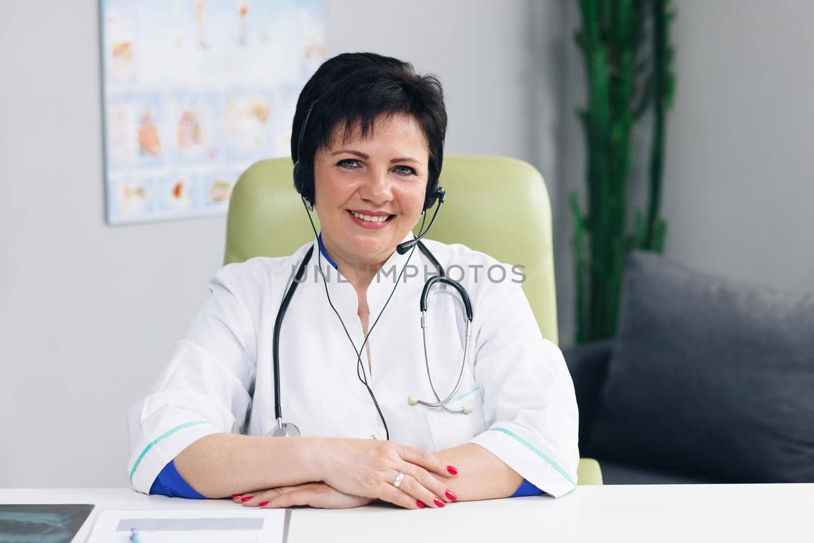 Successful physician in white lab coat wears headset looks at the camera and smiles in hospital office. Telemedicine, telehealth. Modern medecine concept.