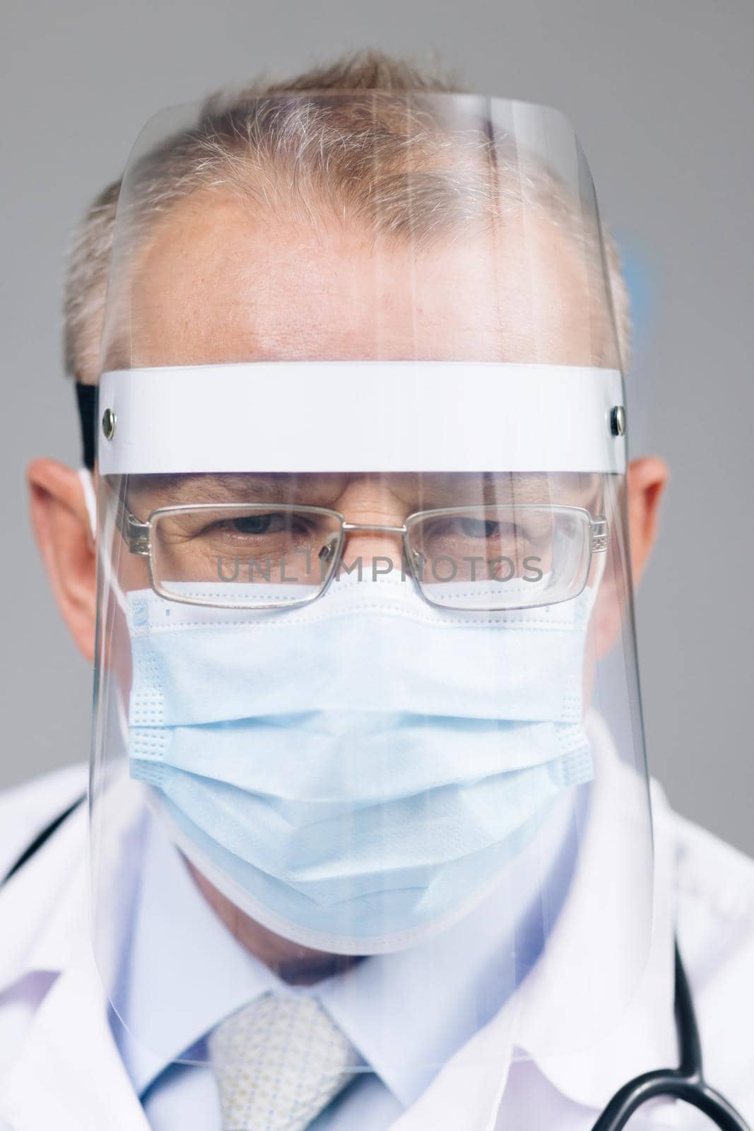 Doctor in Glasses is Wearing a Transparent Protective Face Shield, Mask and Overalls in a Hospital Room. Covid-19 Pandemic Concept About Slow Spread of Infectious Virus. by uflypro