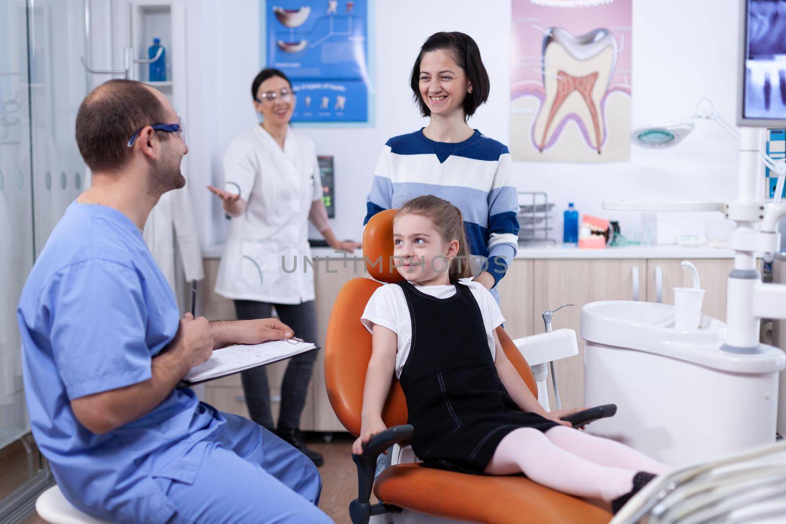 Dentist assistant giving good news to kid parent after teeth examination in dental office. Child with her mother during teeth check up with stomatolog sitting on chair.