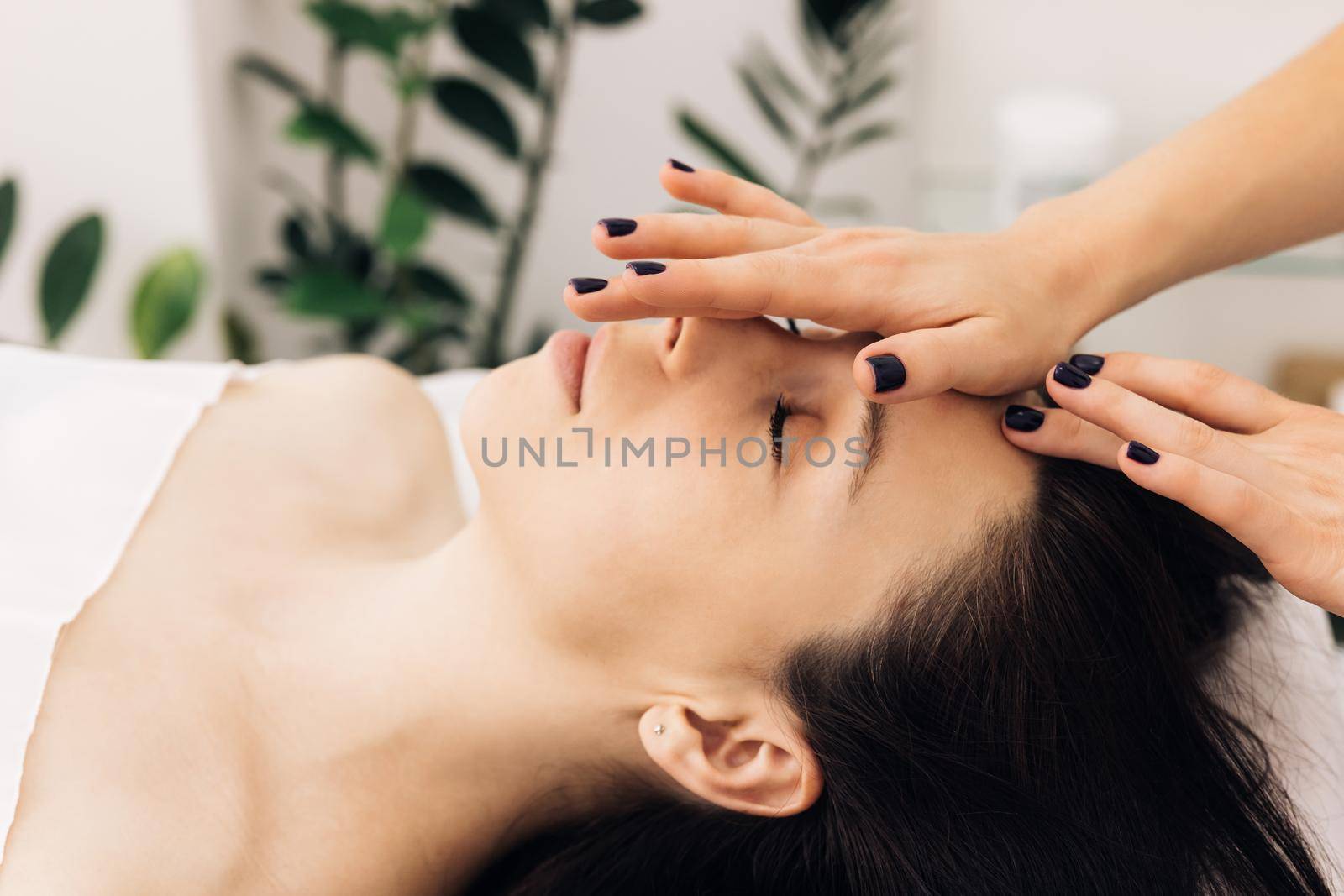 Woman lying on spa bed get facial massage treatment with aroma essential oil skincare from massage therapist at beauty salon. Wellness body massage and face spa concept. by uflypro