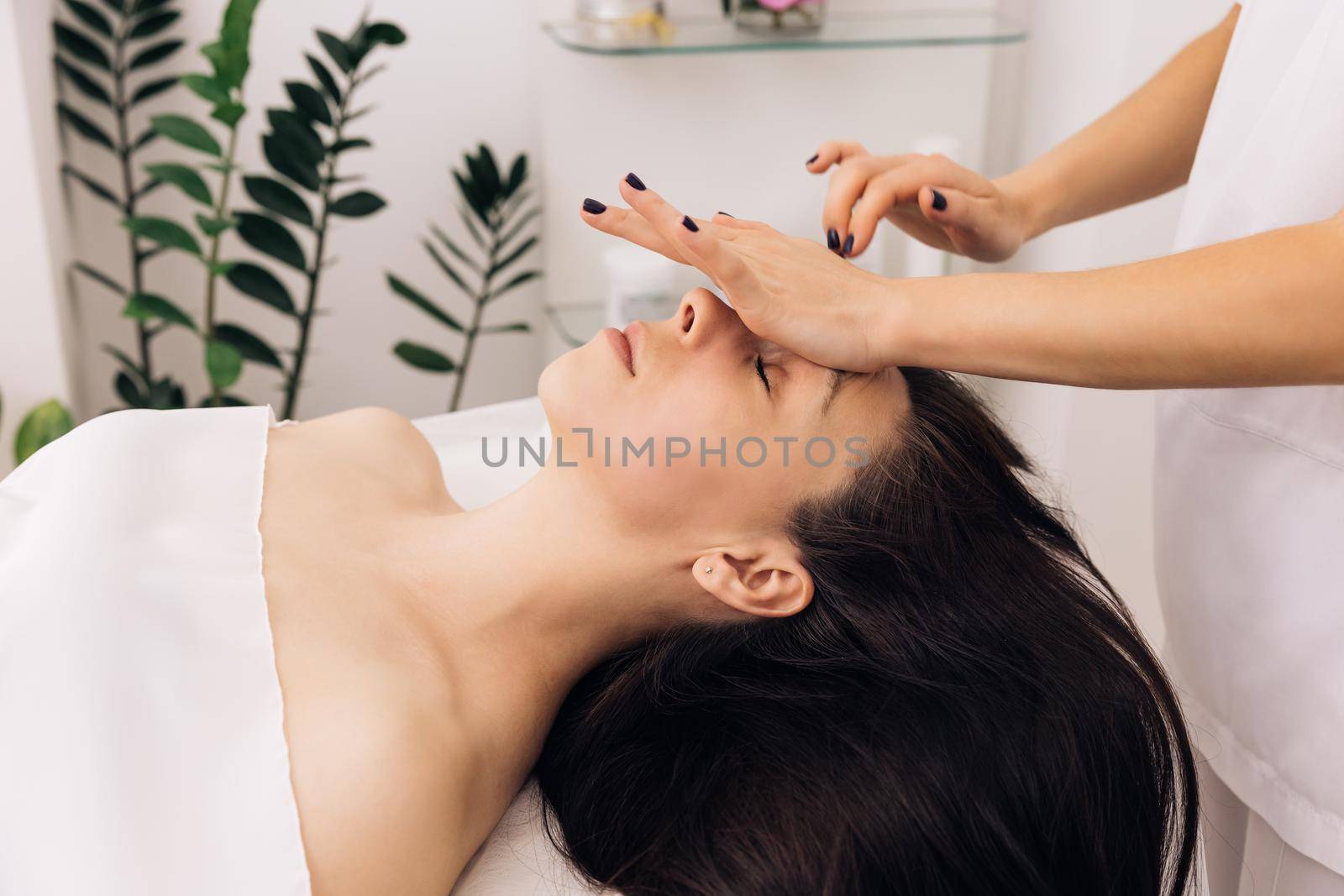 Close up of young girl receiving a facial massage and spa treatment for perfect skin in a luxury wellness center. Caucasian woman lying on spa bed get facial massage from massage therapist at clinic by uflypro