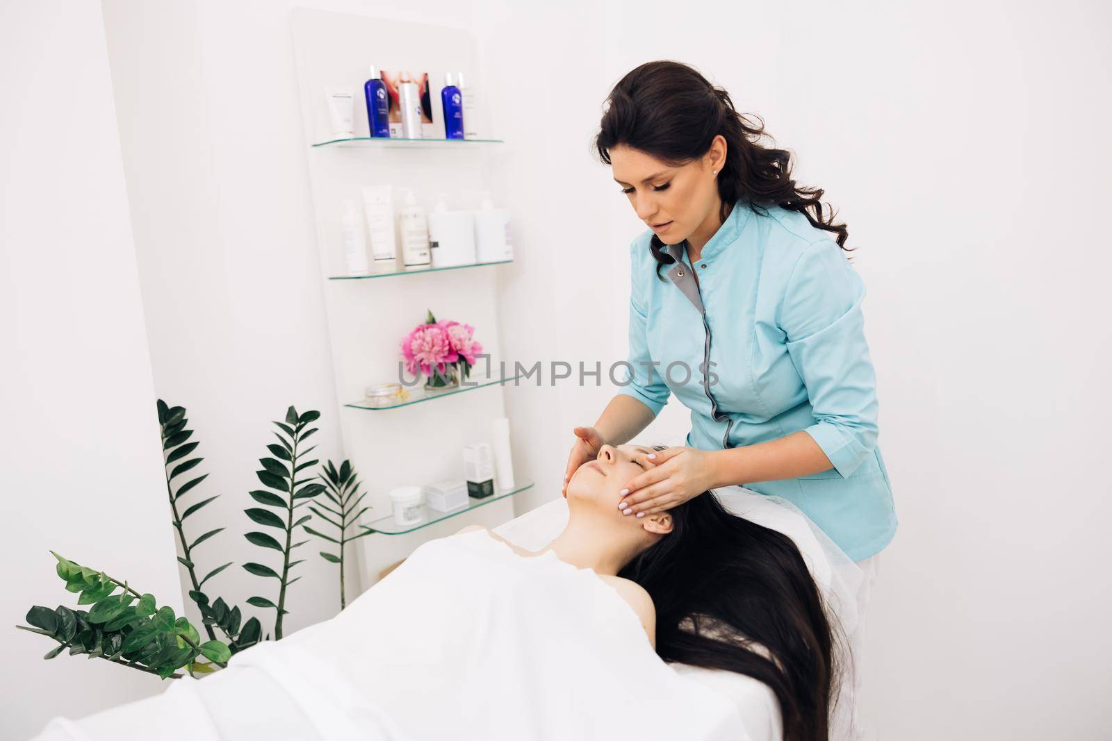 Young woman having massage by a female masseur in blue medical pijama at modern health center. Wellness health concept. Woman relaxing during massage lying on massage table by uflypro