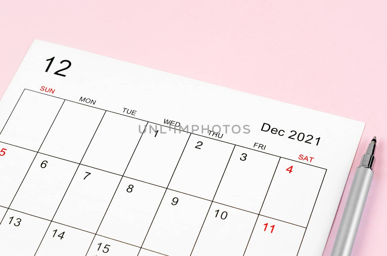 Close up December 2021 calendar sheet with pen on pink background.