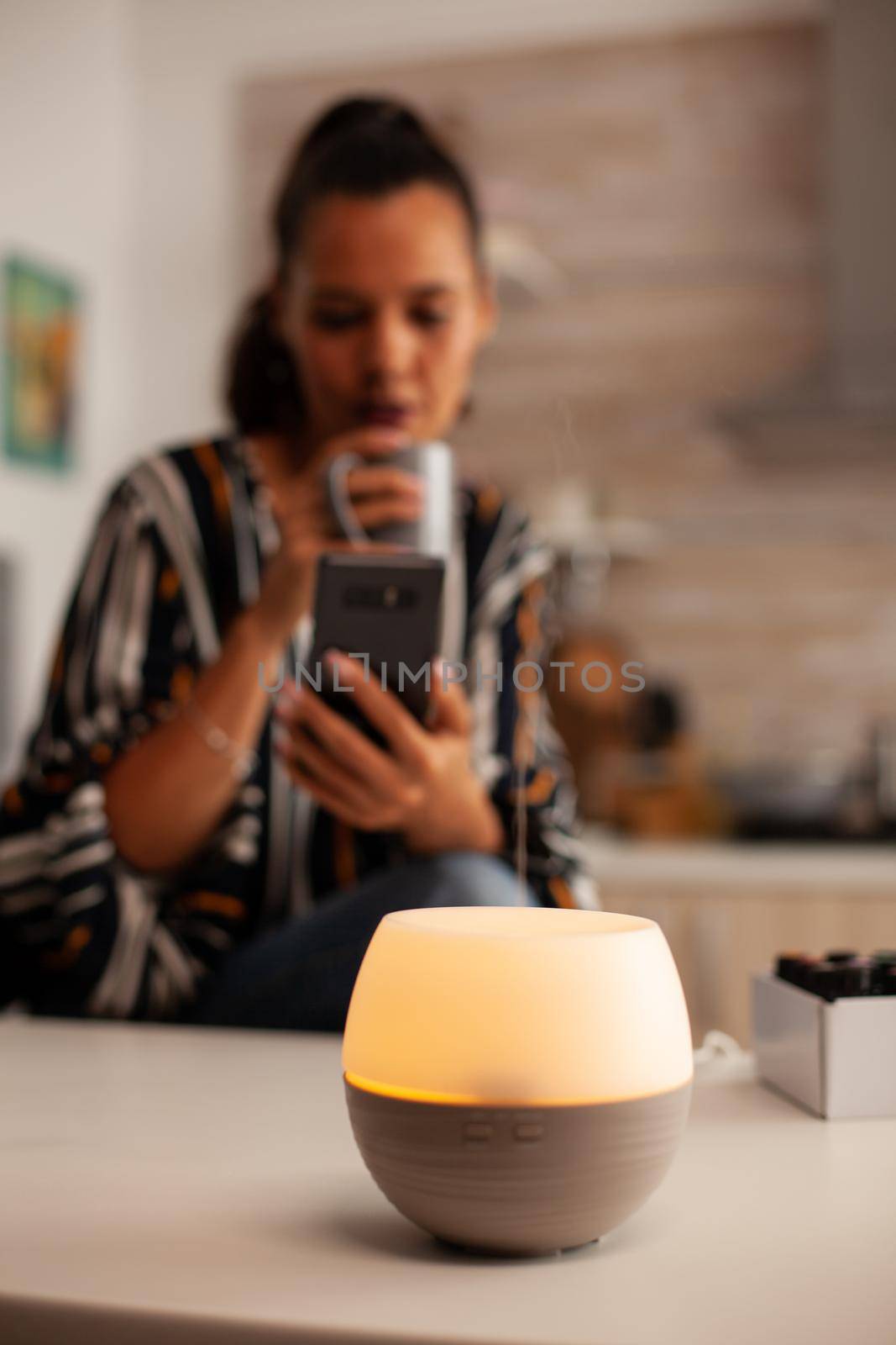 Woman browsing on phone enjoying aromatherapy from essential oil diffuser. Aroma health essence, welness aromatherapy home spa fragrance tranquil theraphy, therapeutic steam, mental health treatment