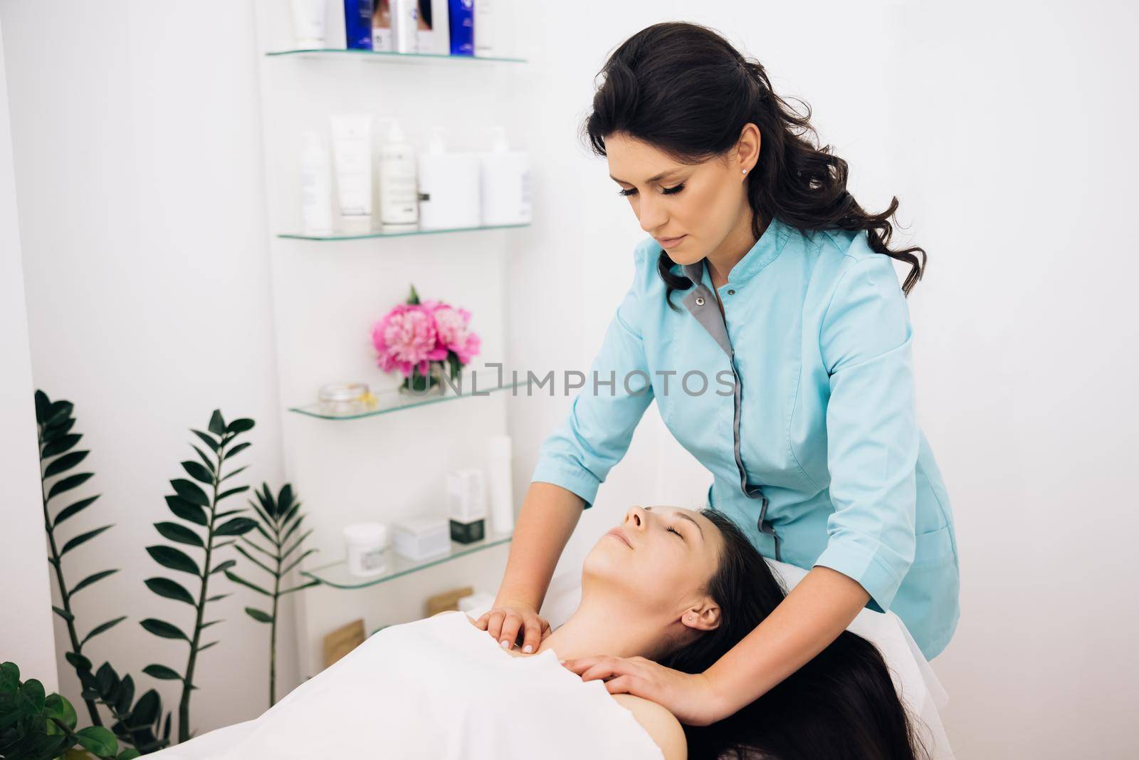 Woman relaxing during massage lying on massage table. Young woman having massage by a female masseur in blue medical pijama at modern health center. Wellness health concept by uflypro