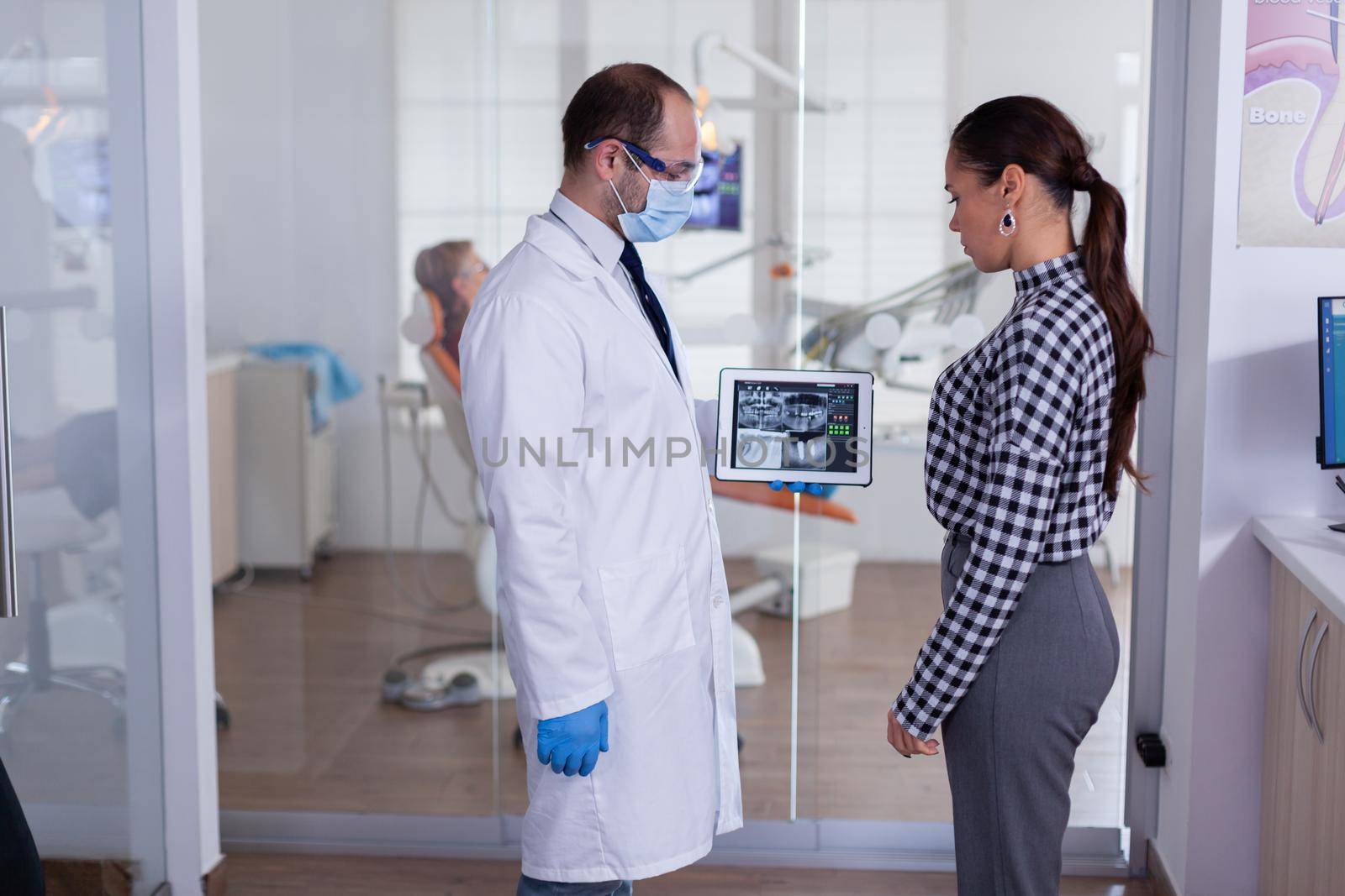 Dentist with face mask showing patient dental x-ray by DCStudio