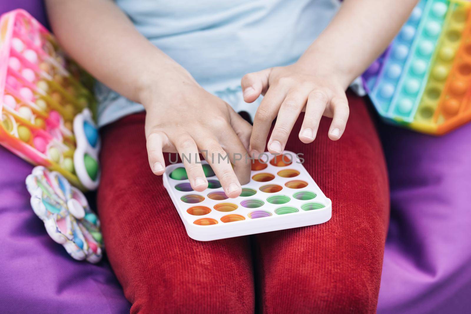 Color silicone anti-stress toy pop it. A new trend for teenagers and children. Hands of a girl in nature playing with a Popit toy close-up. Children's hands play with the rainbow pop it fidget toy.