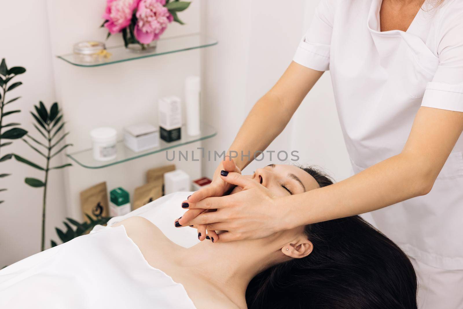 Wellness, stress relief and rejuvenation concept. Relaxed woman lying on spa bed for facial and head massage spa treatment by massage therapist in a luxury spa resort by uflypro