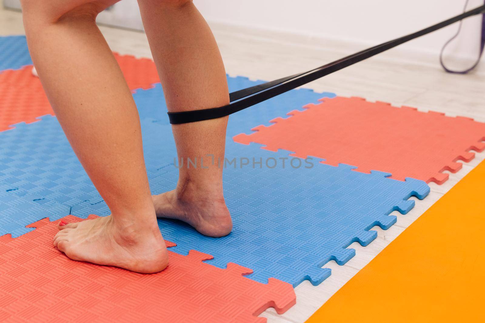 Physiotherapist checking patients leg on a mat on the floor in bright room. physio gives myotherapy using trigger points on athlete woman. Female with elastic bandage doing sport exercises in gym by uflypro