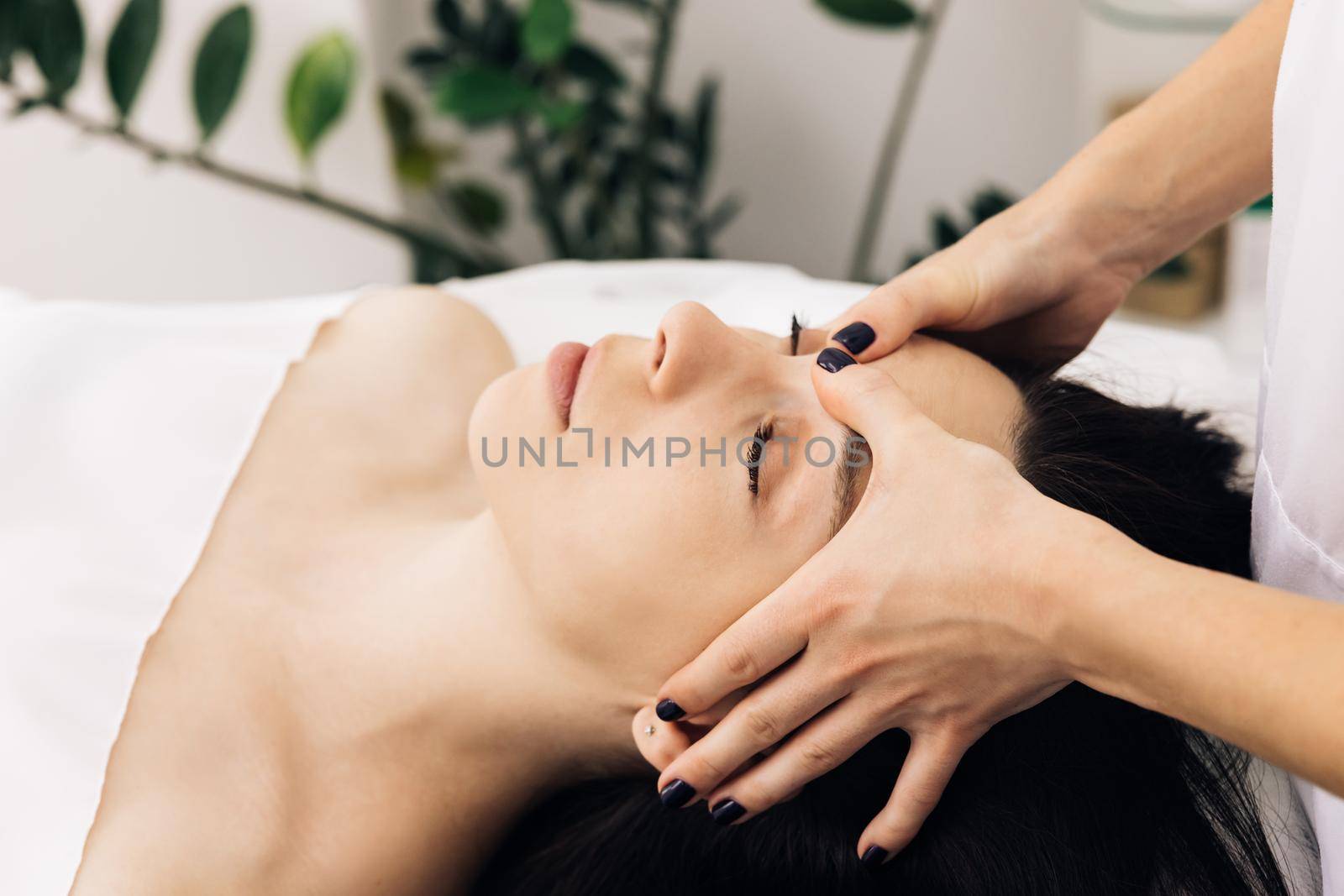 Caucasian woman lying on spa bed get facial massage treatment with aroma essential oil skincare from massage therapist at beauty salon. Wellness body massage and face spa concept