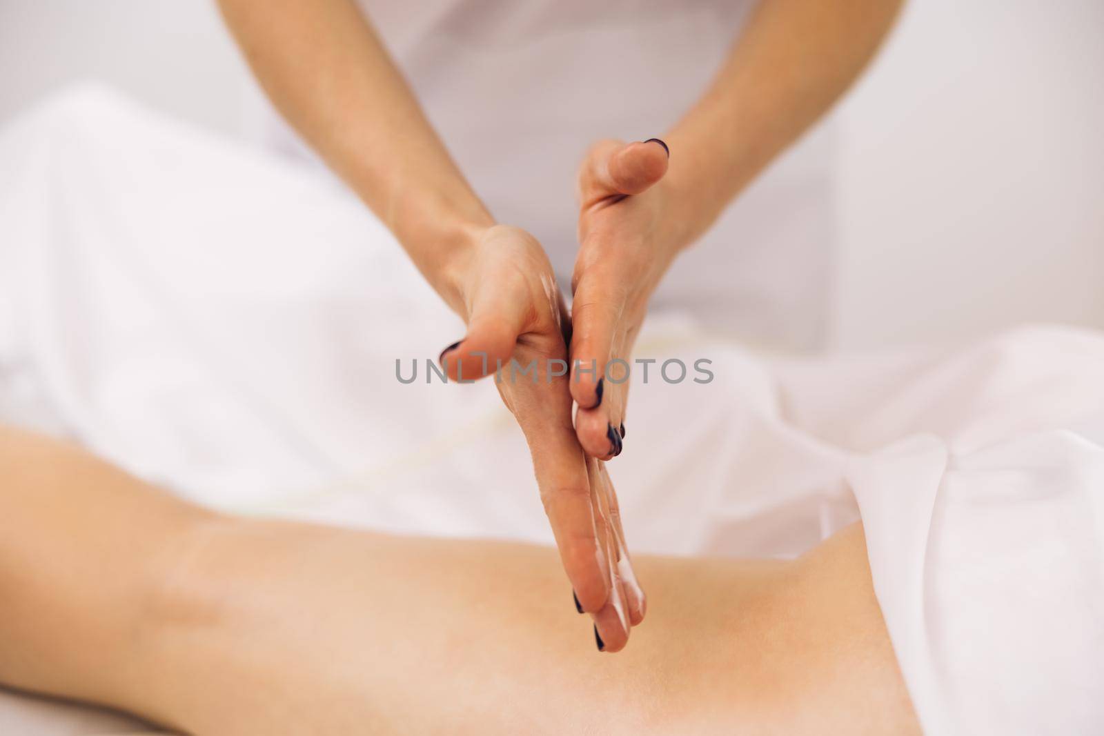 Woman receiving professional body, leg and foot massage and lymphatic drainage in health massage salon. Massage creme treatment. Anti-cellulite massage of hips.