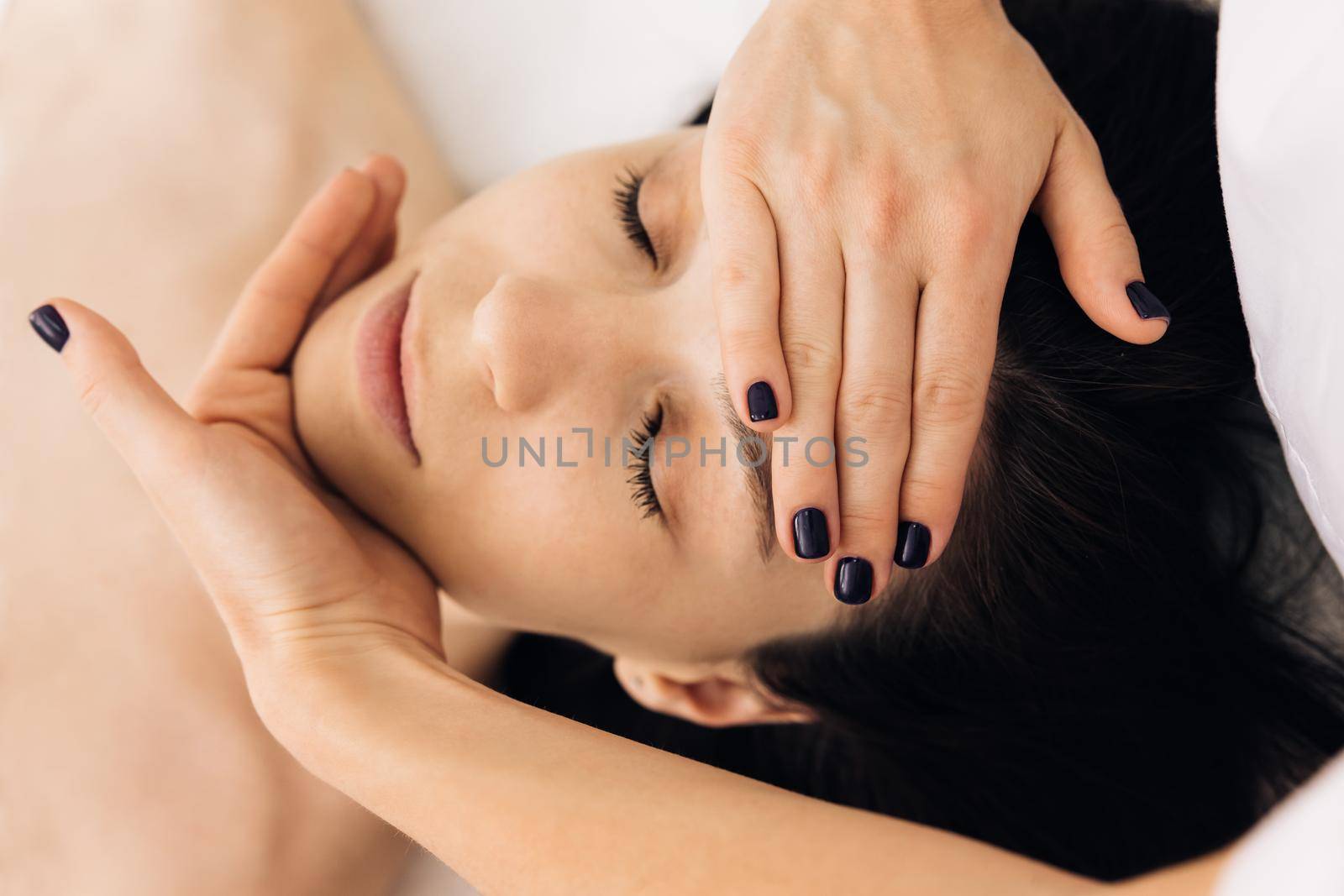 Beautician doctor is applying facial cleansing foam on woman's face massaging skin in cosmetology clinic. Cosmetologist making skin care procedure in beauty salon, portrait of girl closeup by uflypro