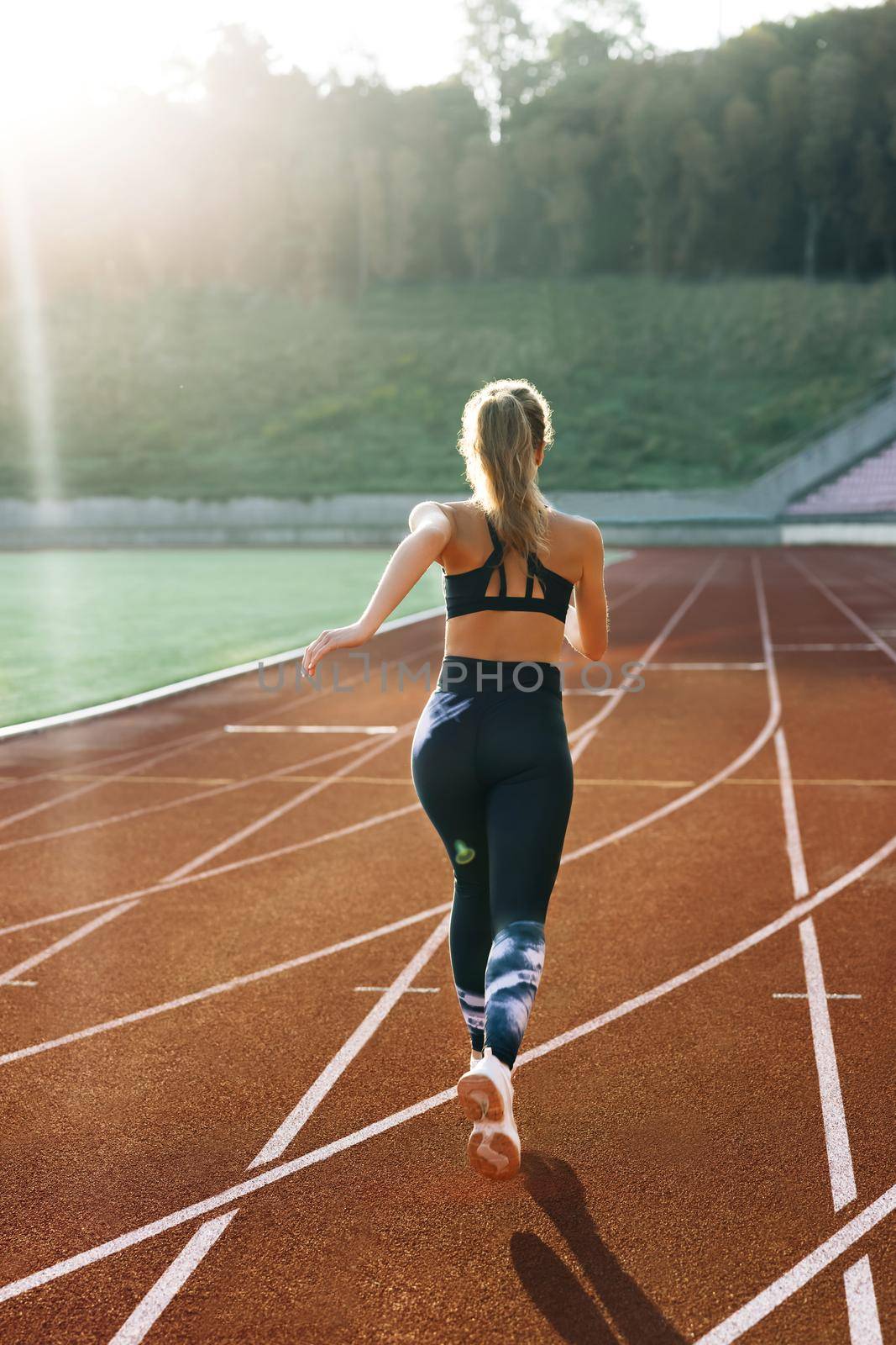 Rear view of Athlete Woman Running Fast at Track in the Morning Light , Training Hard, Getting Ready for Race Competition or Marathon. Fit Girl in Black Sportswear Jogging on a Running Track.