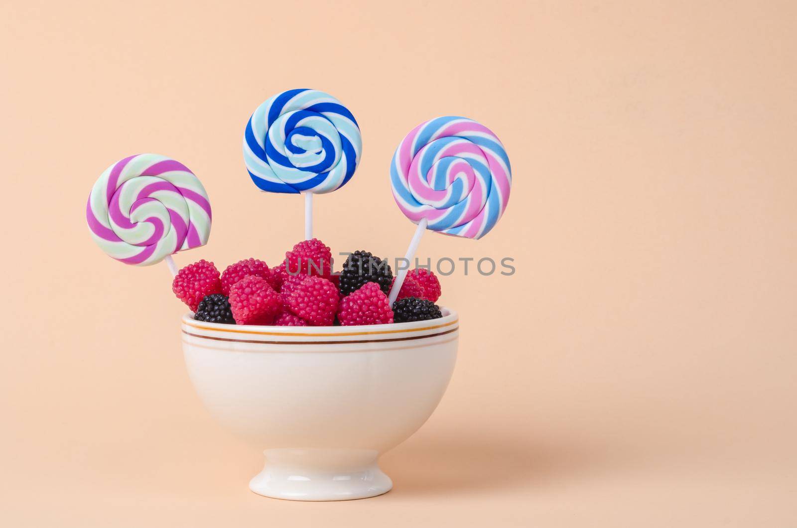 Sweet gummy in cup and marshmallow on pastel orange background.