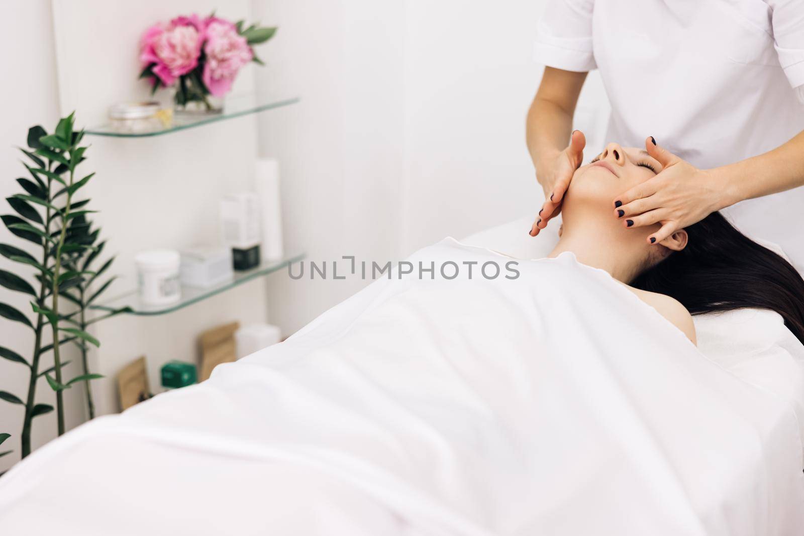 Relaxed woman lying on spa bed for facial and head massage spa treatment by massage therapist in a luxury spa resort. Wellness, stress relief and rejuvenation concept.