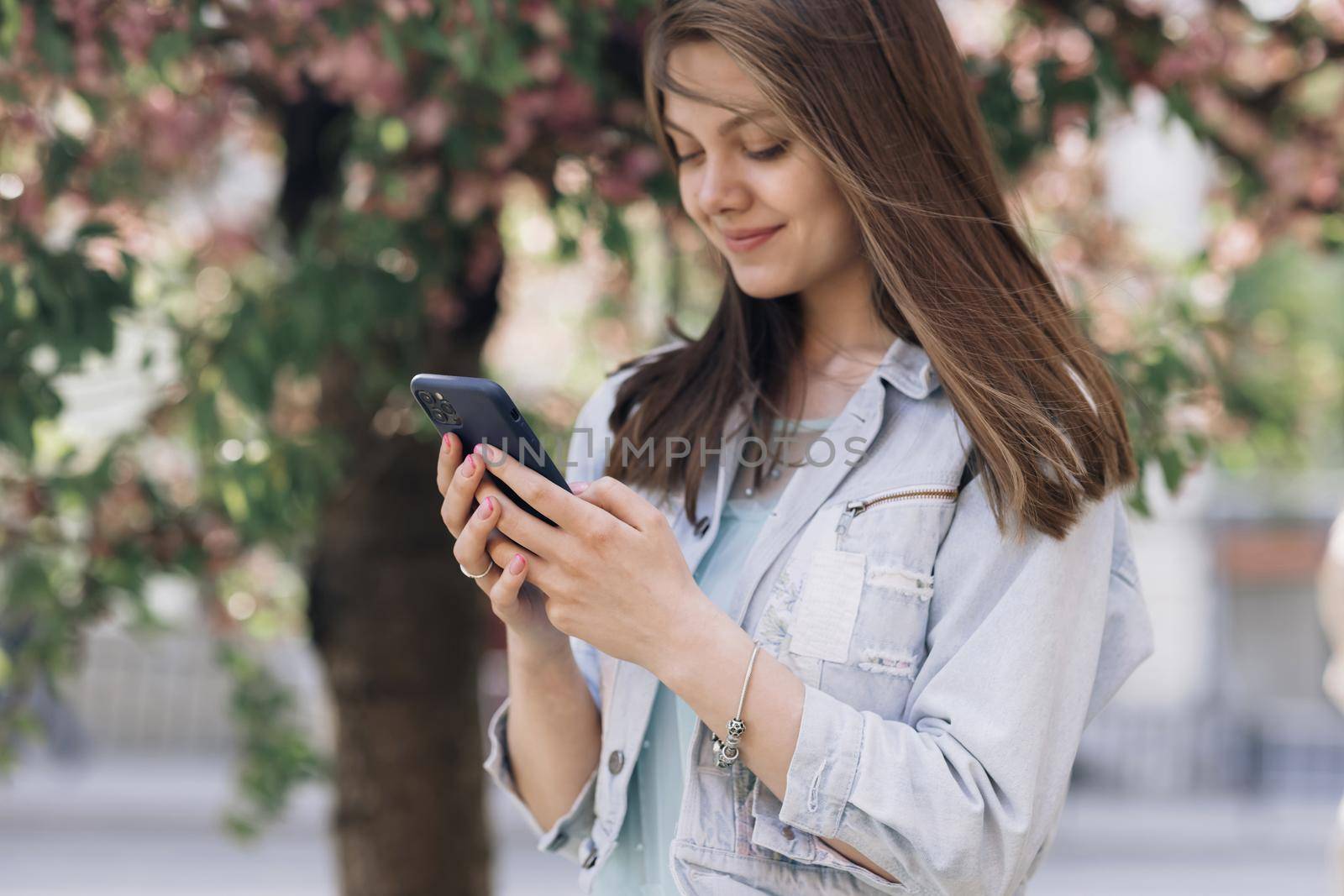 Cheerful woman looking at mobile phone in the street urban people with cellphone in hand. Pretty summer woman in white dress walks down the street looking at her mobile phone. by uflypro