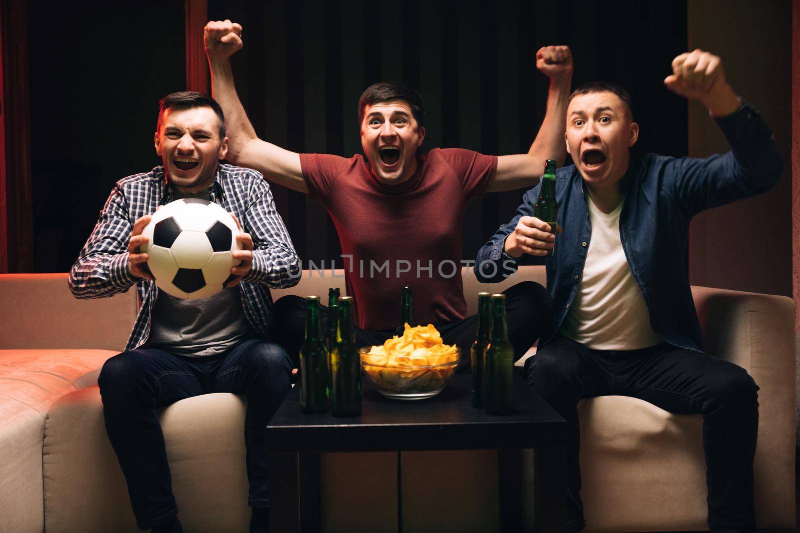 Loyal football fans supporting their team. Young male sport fans shout watching football game together at home. Expressing, screaming and emotion.