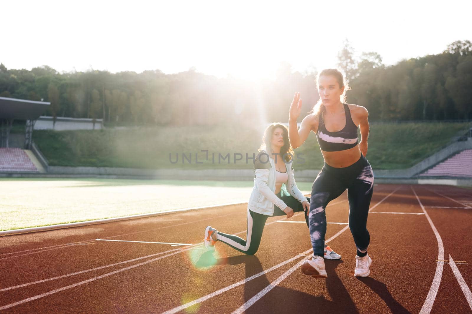Female athlete training with personal trainer at running track in the morning light. Active fitness woman runner jogging in sunny track summer day outdoors. Jogger activity. Sportswoman.