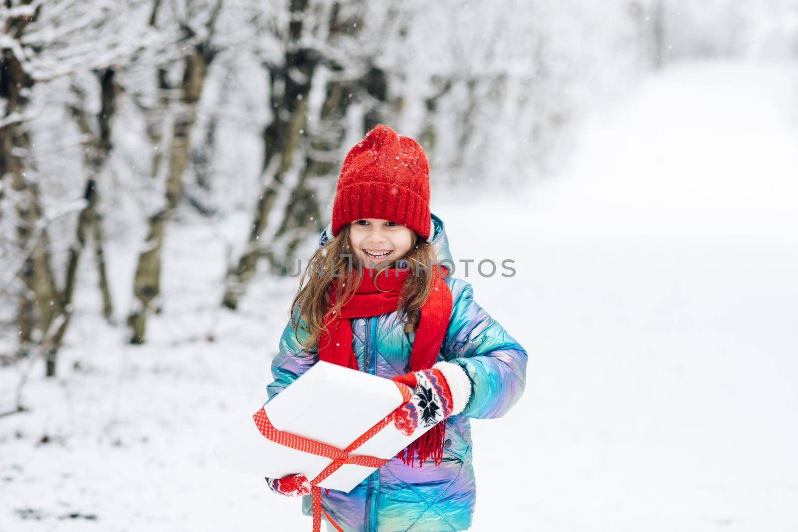 Little girl with christmas box gift in winter outdoors on Xmas eve. Happy Little caucasian girl smile and holding gift box in Christmas day. Child holding gift box and surprise face.