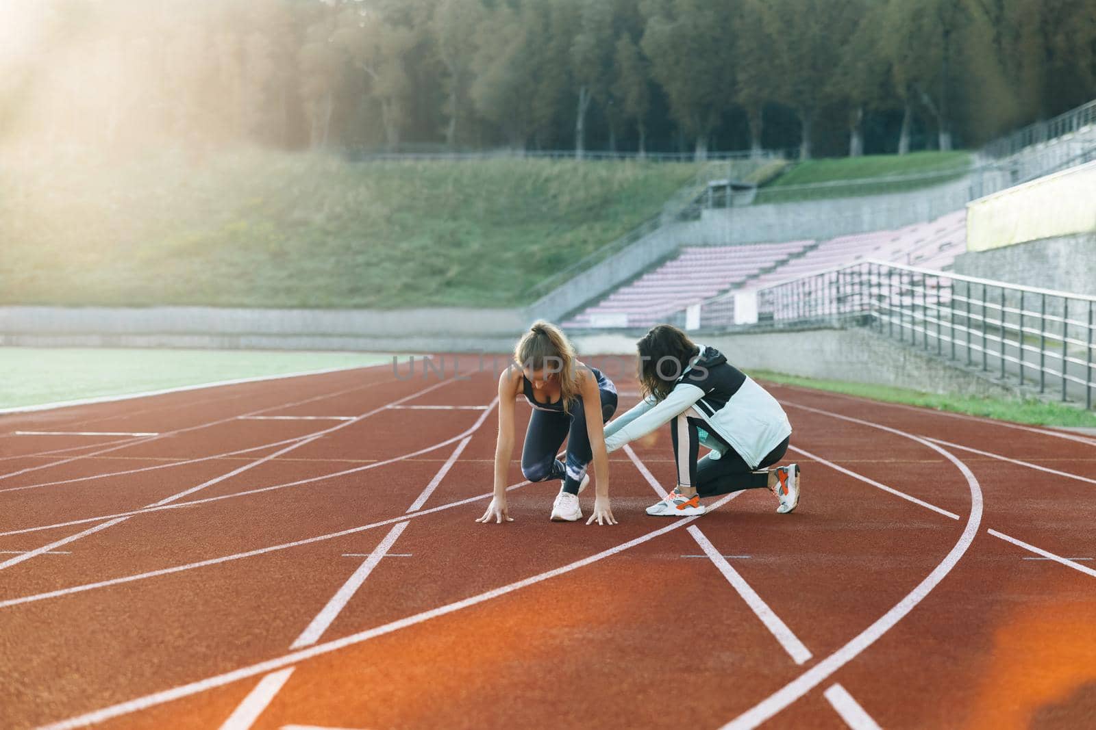 Female athlete on track. Young athlete exercises with personal trainer standing on start on stadium, then rushing forward, getting ready for competition. Exercising strength, cardio and power. by uflypro