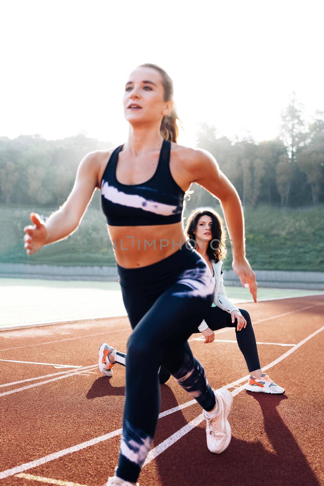 Athlete exercises with personal trainer standing on start on stadium, then rushing forward, getting ready for competition. Female athlete on track. Exercising strength, cardio and power