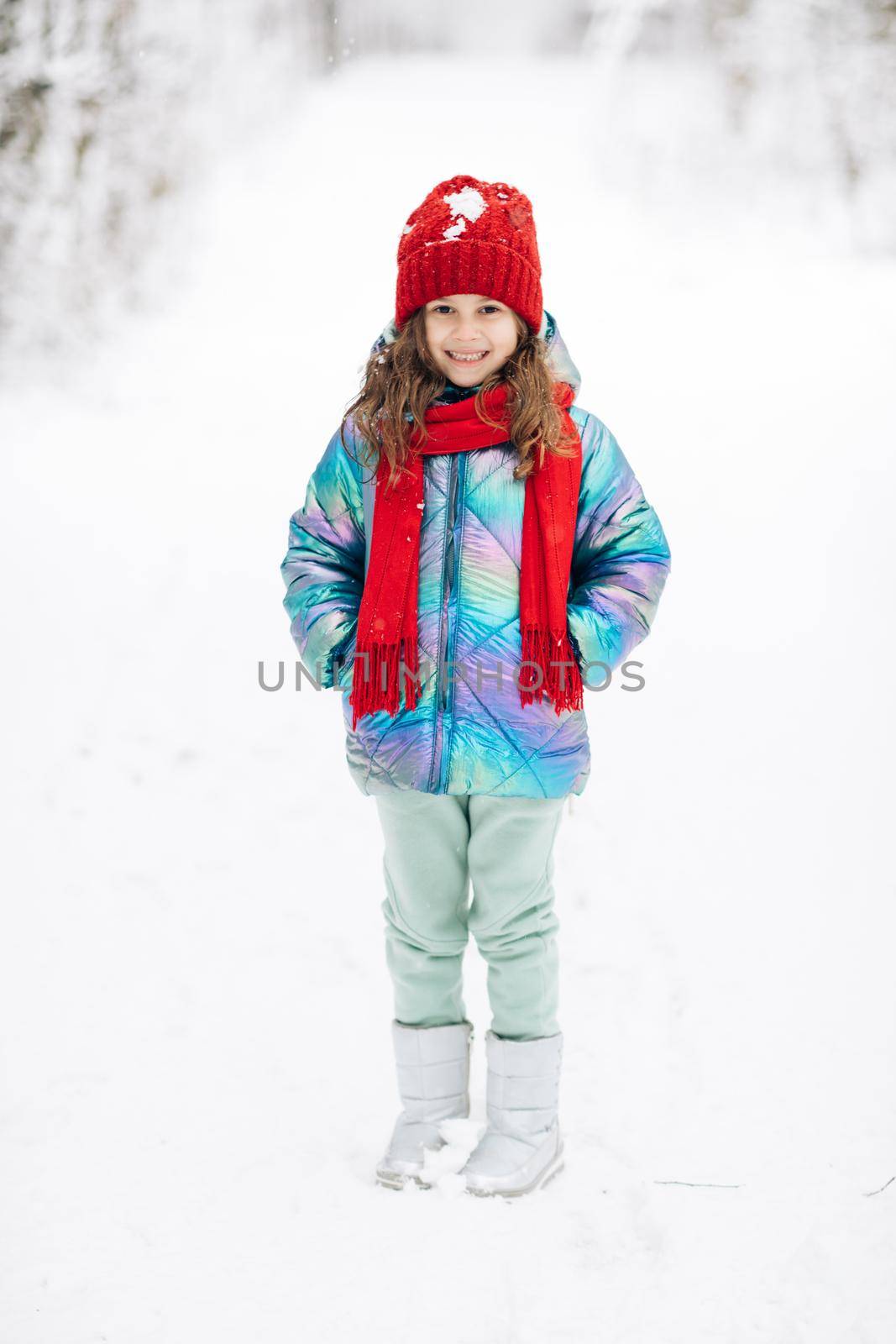 Portrait Little Child Girl Smiling Looking at Camera Standing into Park Outdoor. Winter time, happiness concept. Snowing weather. Carefree childhood.