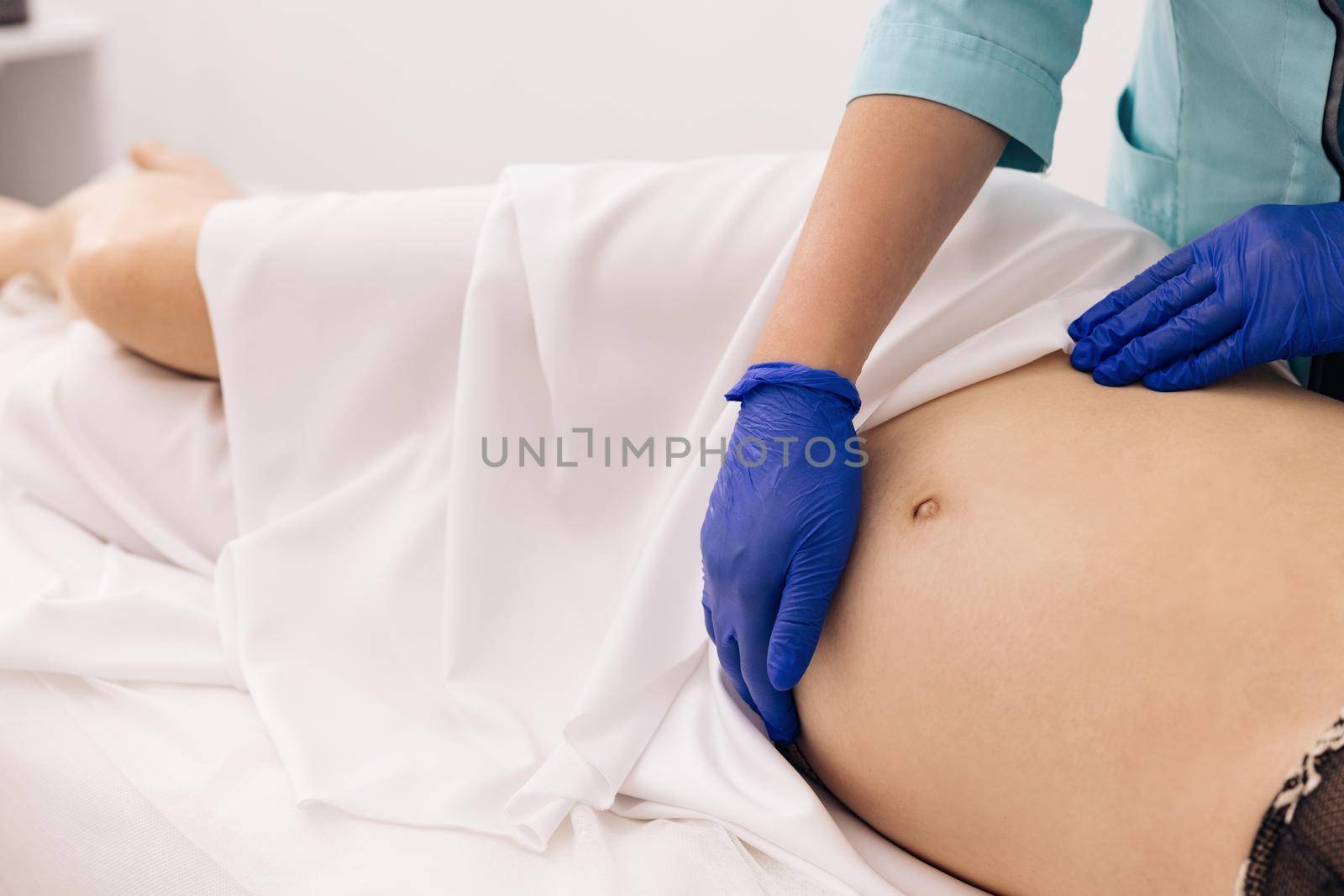 Pregnant woman visit gynecologist doctor at hospital or medical clinic. Pregnancy and maternity healthcare concept. Physiotherapist woman massaging tummy on pregnant woman on a stretcher. by uflypro