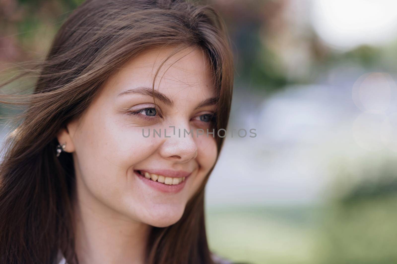 Close up portrait Smiling attractive young adult woman model, happy beautiful 20s brunette lady pretty face dental smile posing stand alone at park on a background of sakura trees.