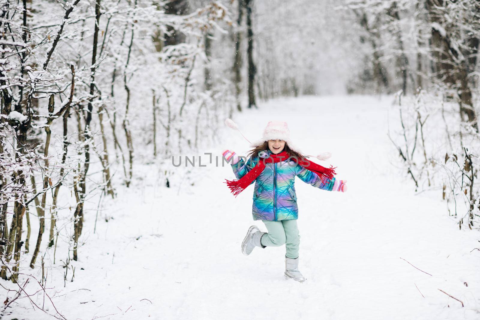 Funny laughing child girl running in a beautiful snowy park. Happy girl playing on a winter walk in nature. Expressing positivity, true brightful emotions, smiling.